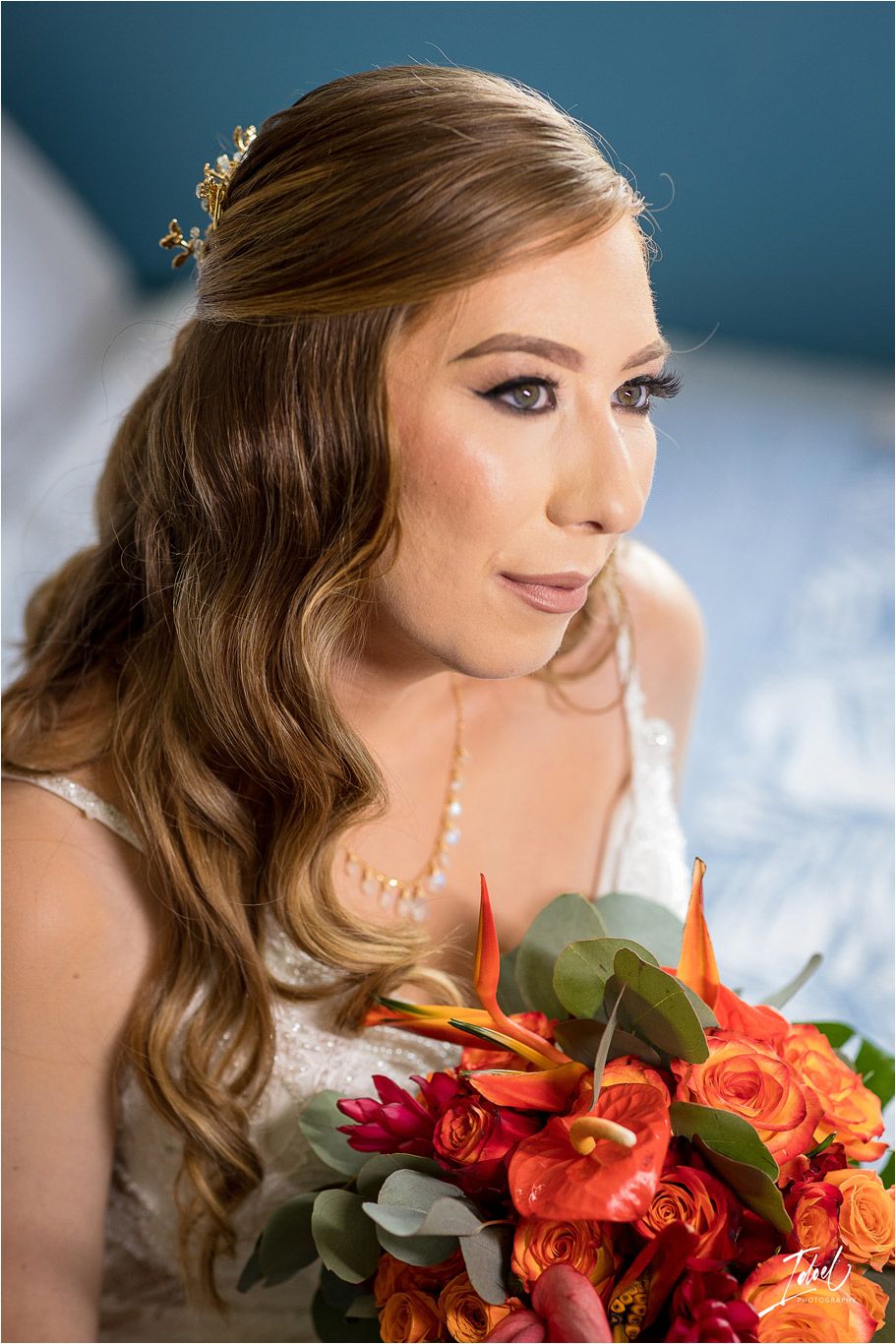 Close-up bridal portrait with colorful bouquet against blue wall.