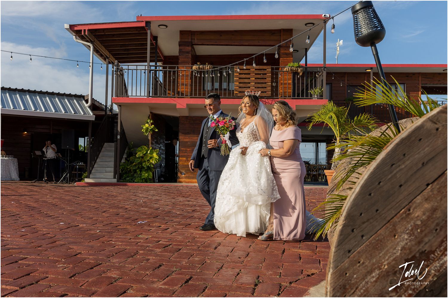Wedding party walking down brick steps at an outdoor venue with red accents and palm trees.