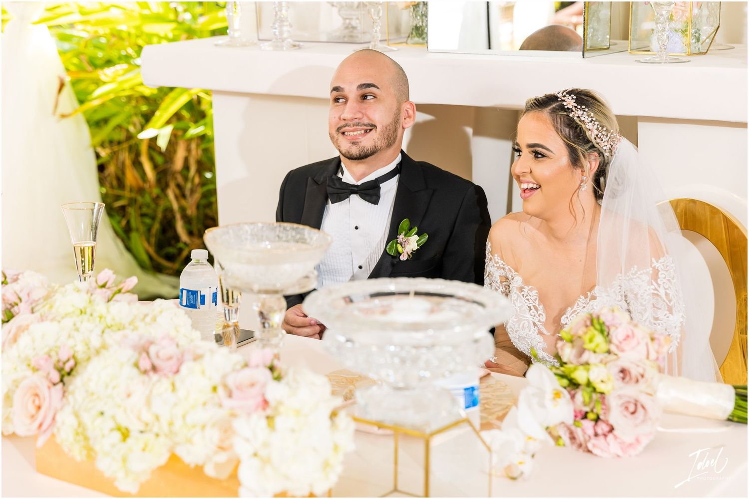 Newlyweds share joyful expressions while seated at their reception table with elegant decorations.