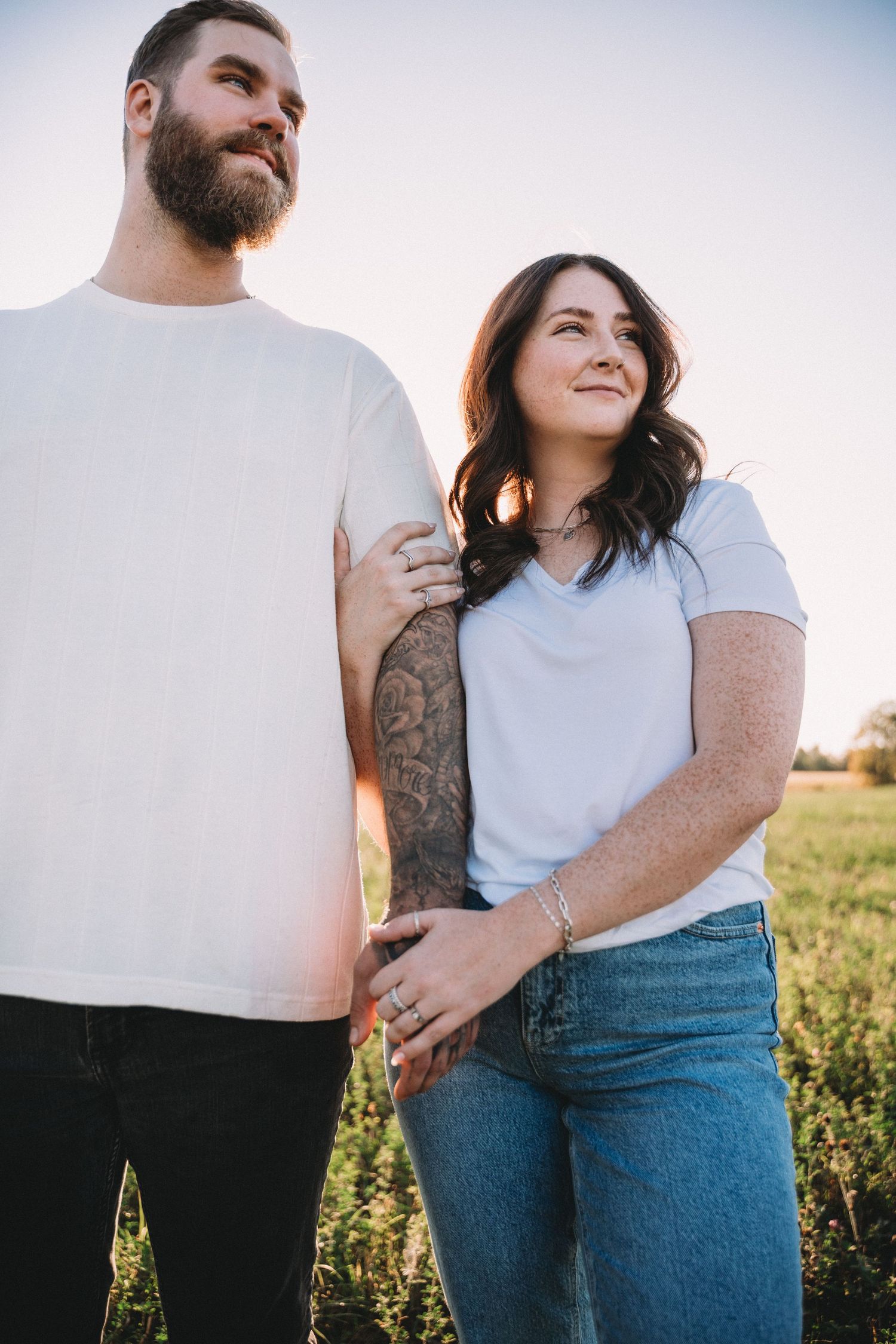 Intimate couple portrait showing casual outfits and tattoos against a bright outdoor backdrop.