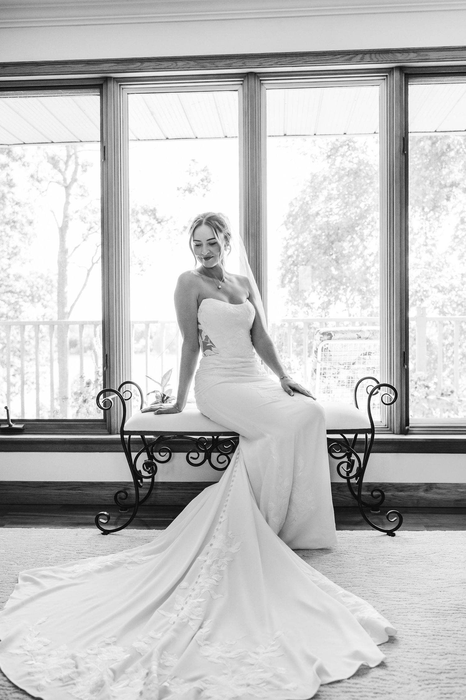 Elegant white wedding dress with flowing train displayed in a sunlit room with iron benches.