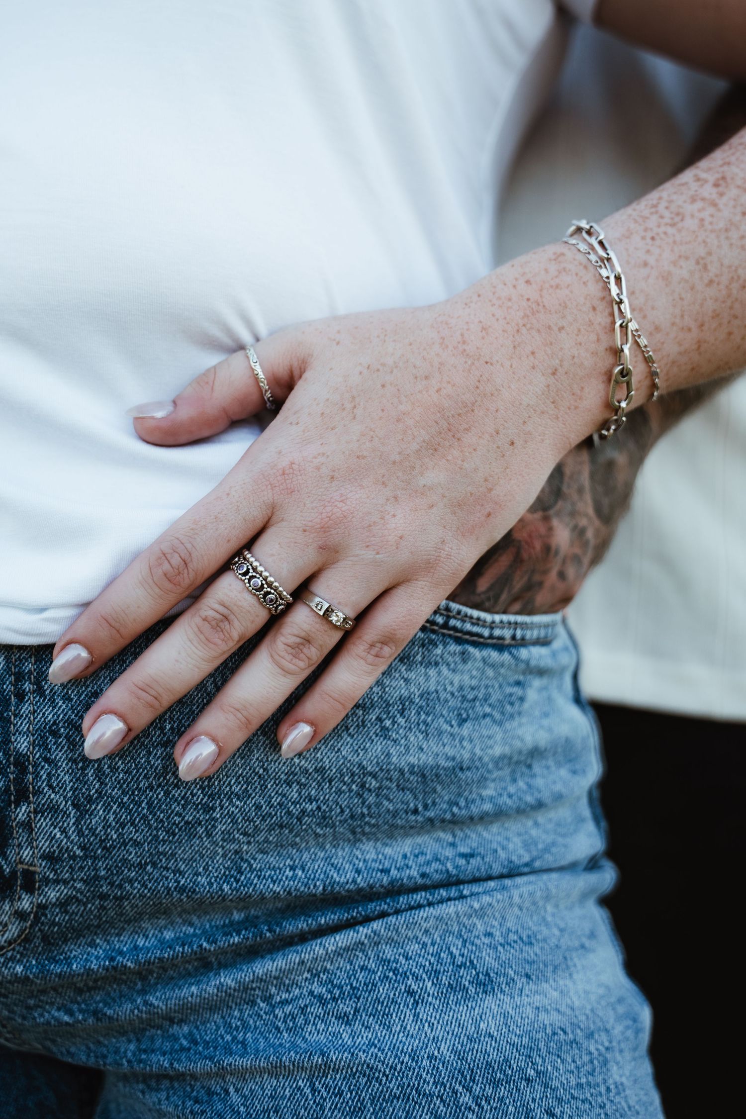 Close-up of hands wearing rings resting against denim fabric.