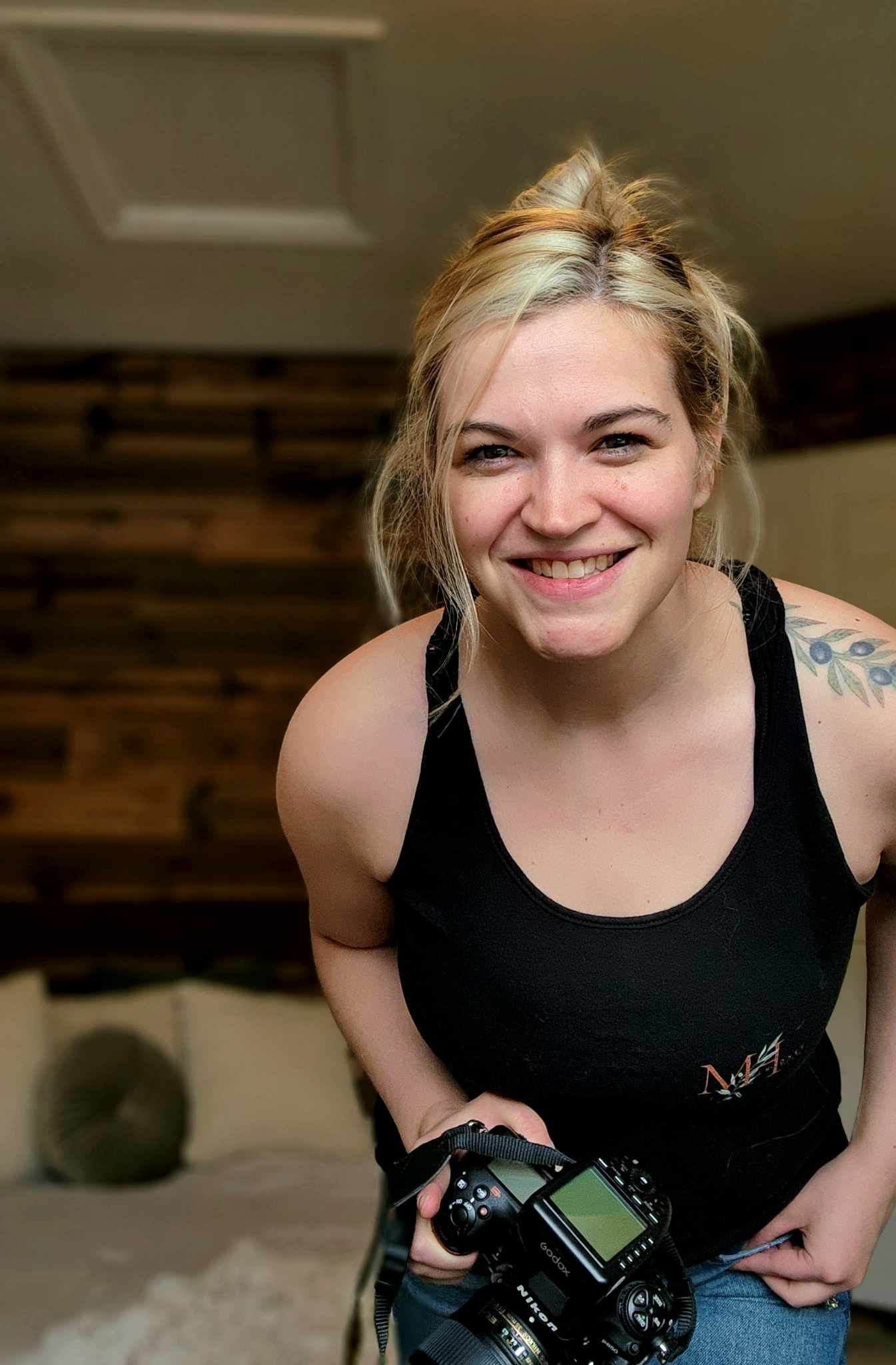 Photographer in black tank top holding camera with natural indoor lighting.