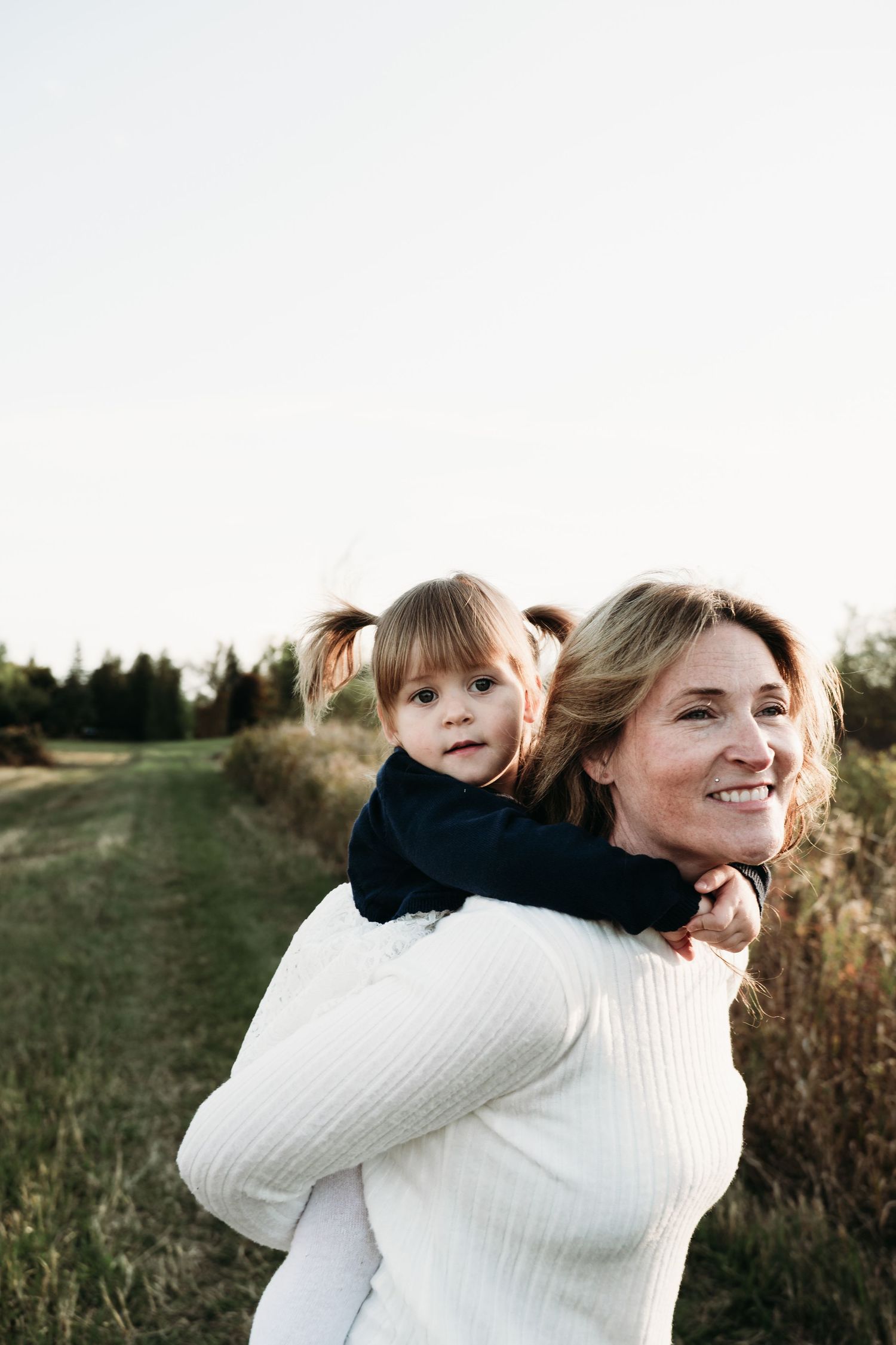A person in a white sweater carries a small child on their back while walking outdoors.
