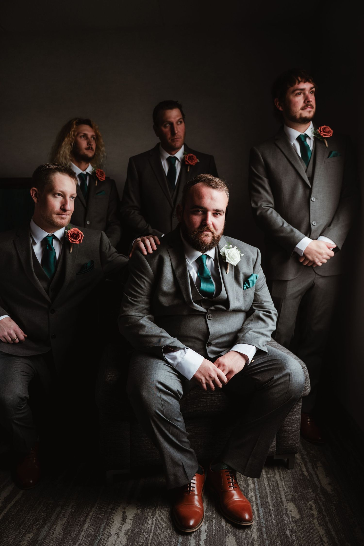 Groomsmen in dark suits sitting in dramatic low-key lighting with brown leather shoes.