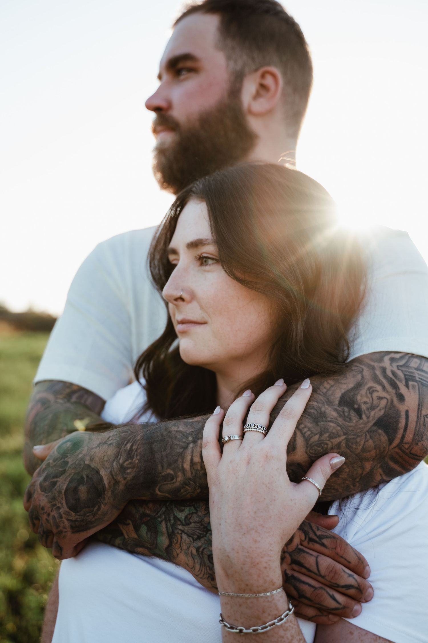 Intimate portrait showing tattooed arms and gentle embrace in golden sunlight.