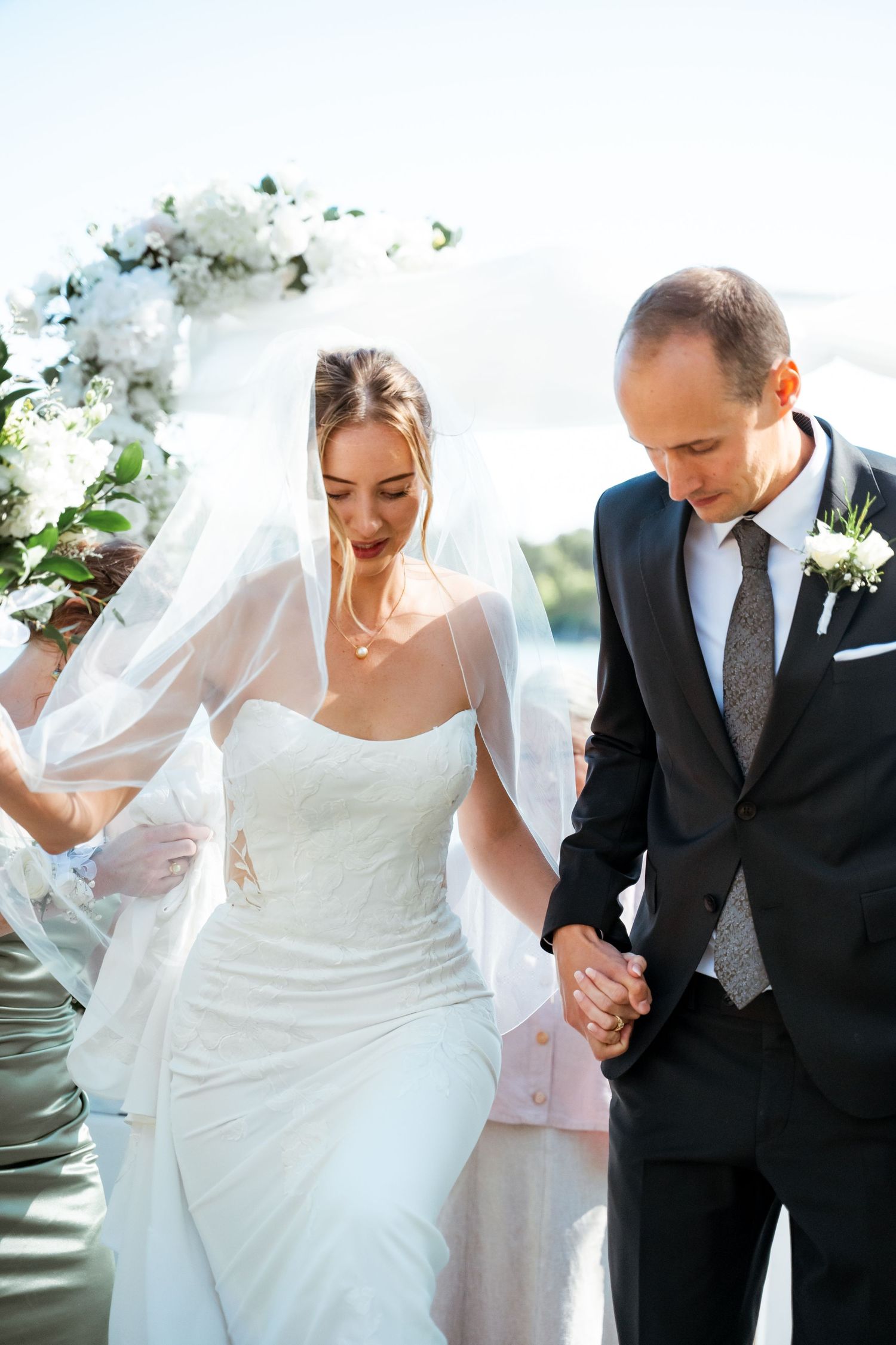 A romantic wedding moment under a floral arch with a flowing veil and elegant attire.