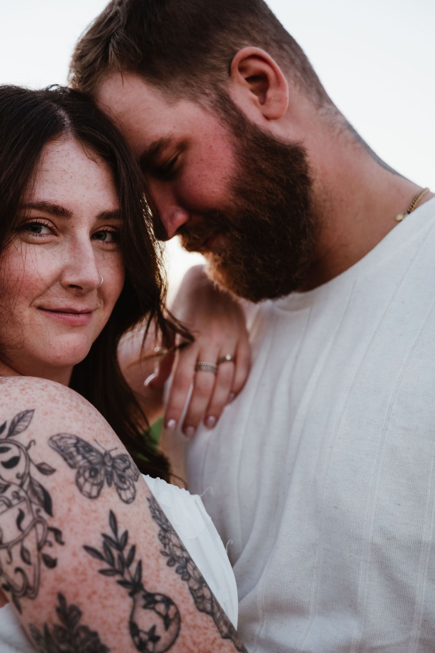 Close-up portrait of couple sharing intimate moment with visible floral tattoos.