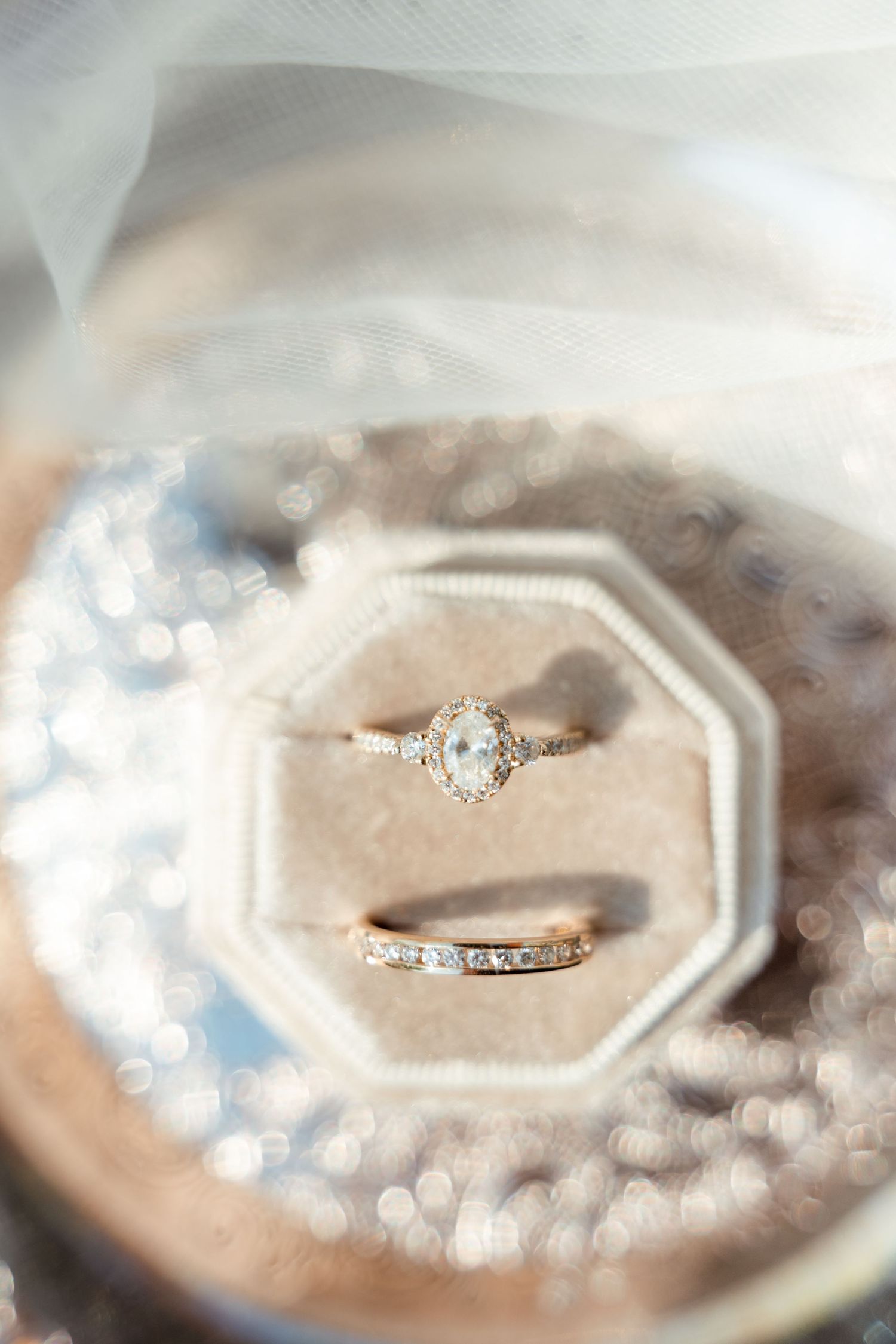 Delicate engagement and wedding rings displayed on a textured surface with soft bokeh lighting effects.