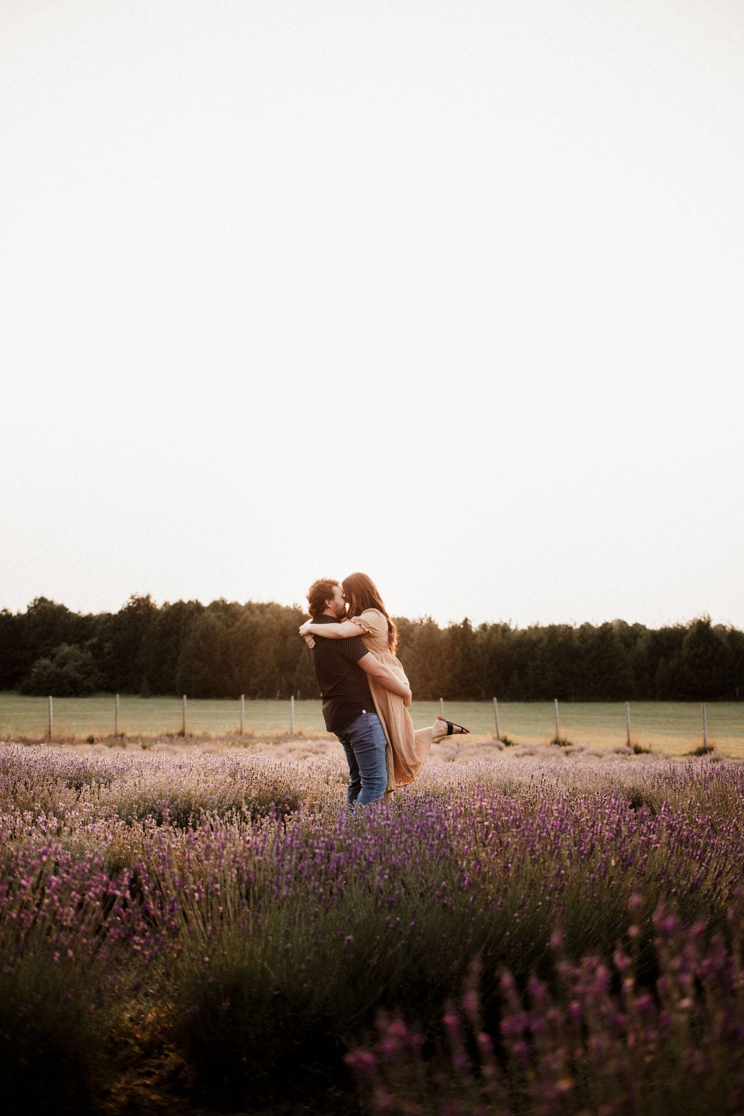 Silhouetted couple sharing tender moments in lavender field at sunset.