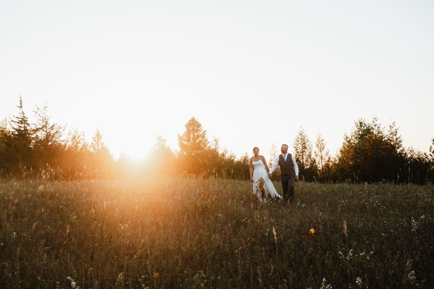 Silhouettes of a couple embrace in a meadow during golden hour with sunlight streaming behind them.