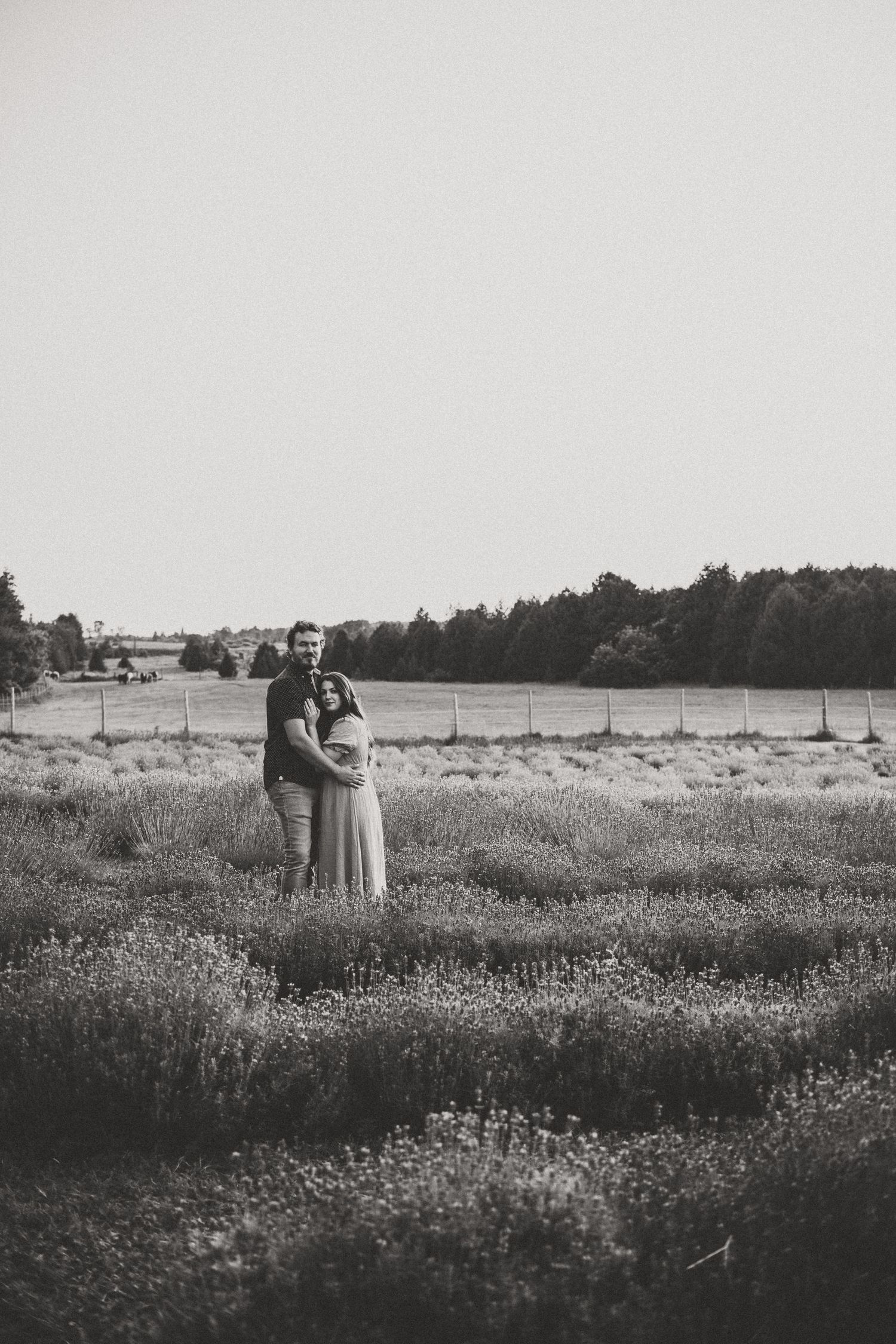 Black and white photograph of couple embracing in a wildflower meadow.