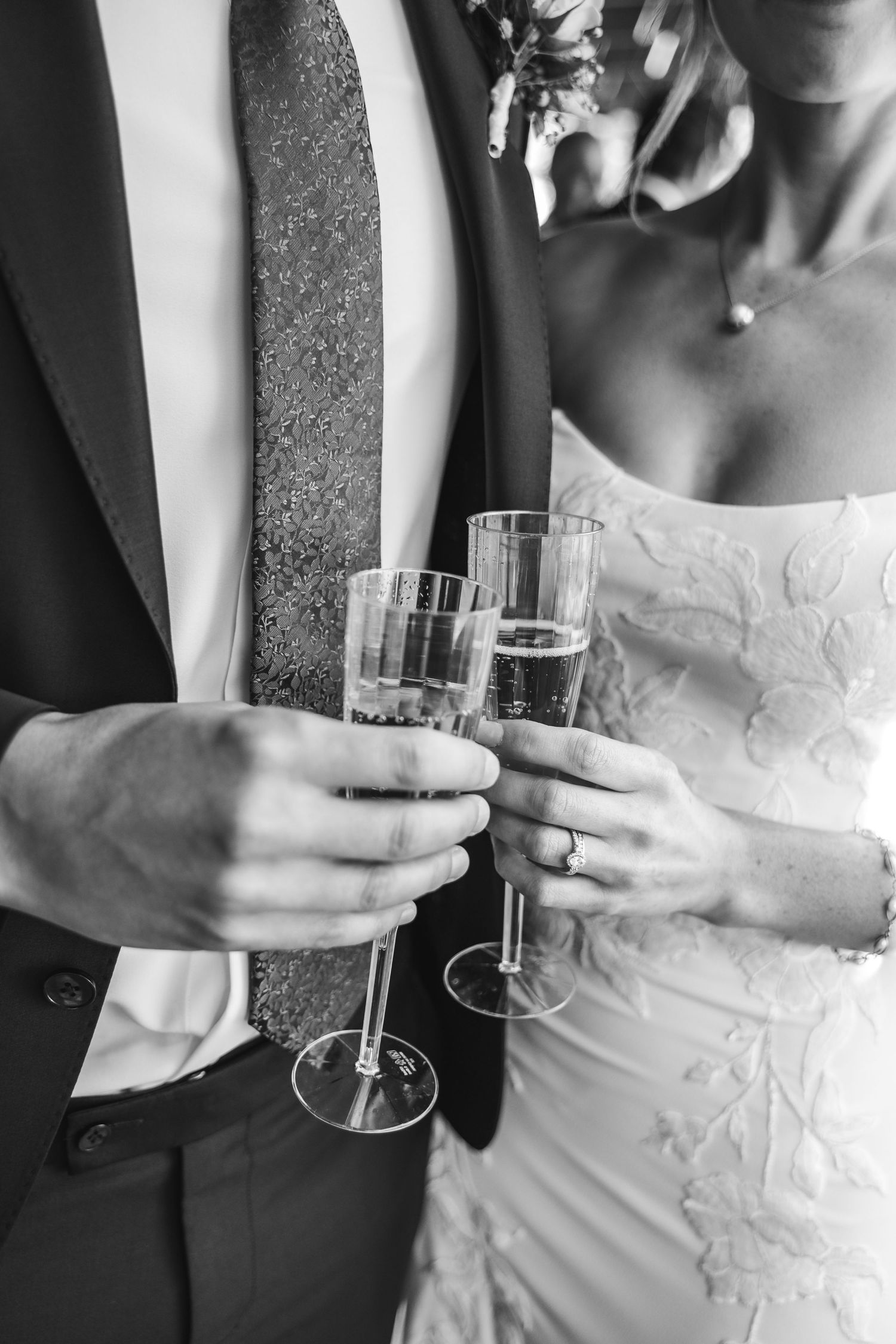 Black and white detail shots of champagne glasses held by couple in formal attire.