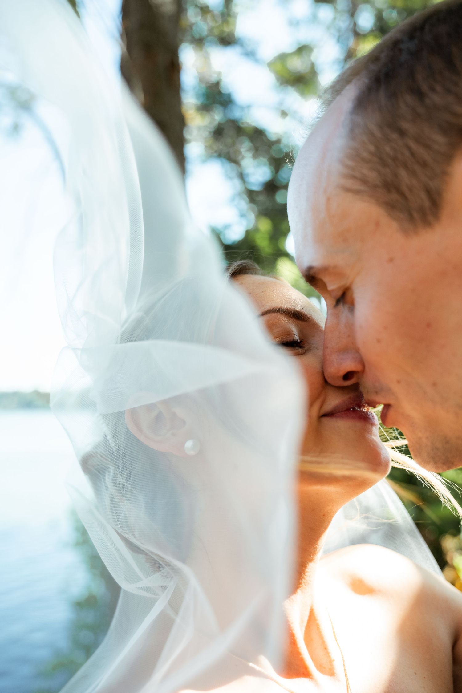 Romantic wedding moment captured through delicate white veil in natural sunlight.