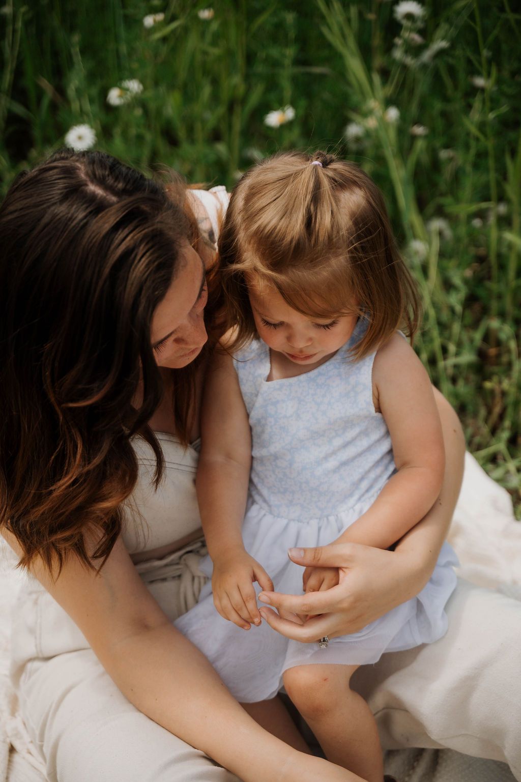Tender moment between parent and child sitting among wildflowers in white summer dresses.