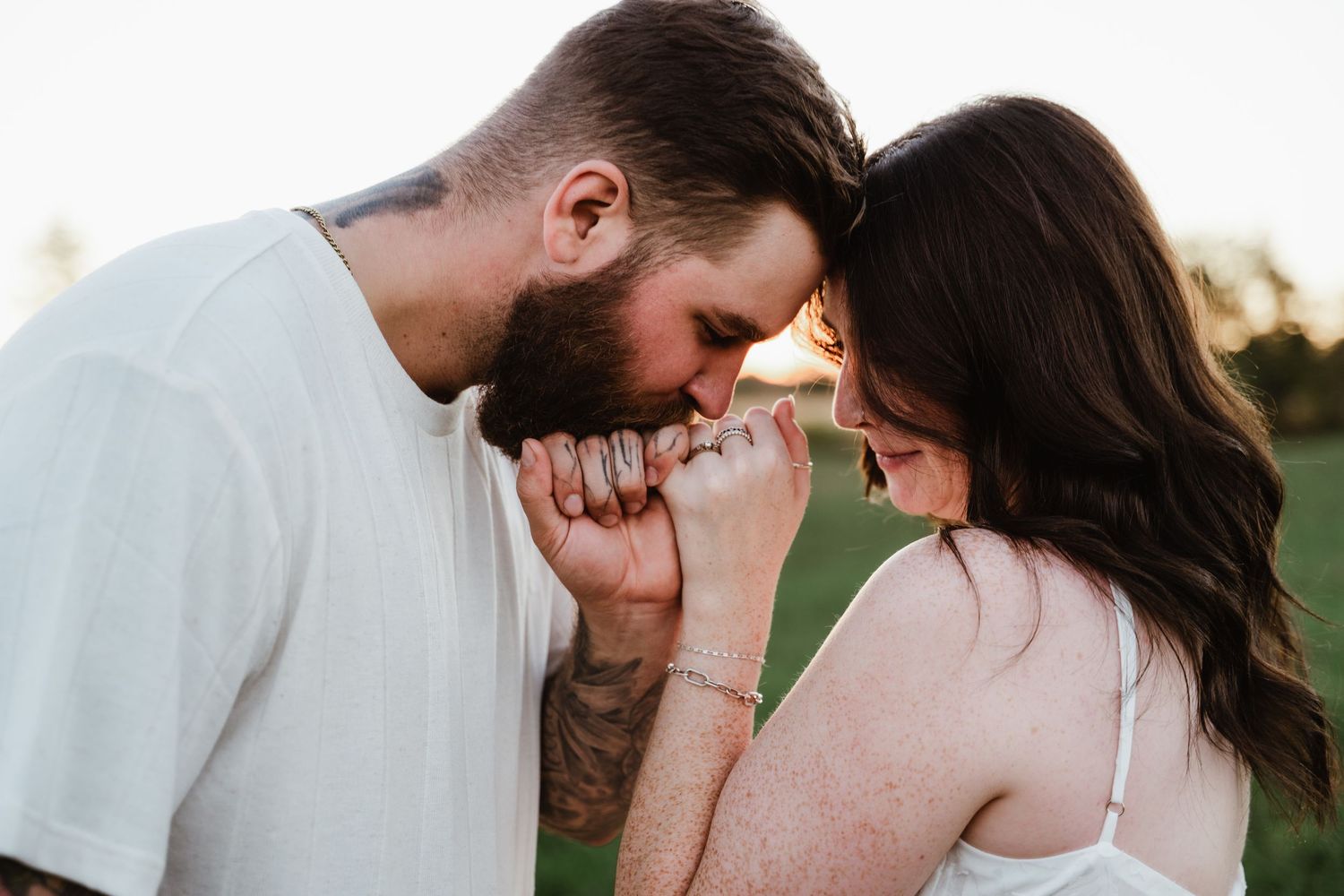 Intimate couple embraces in soft natural light showing visible tattoos and tender connection.