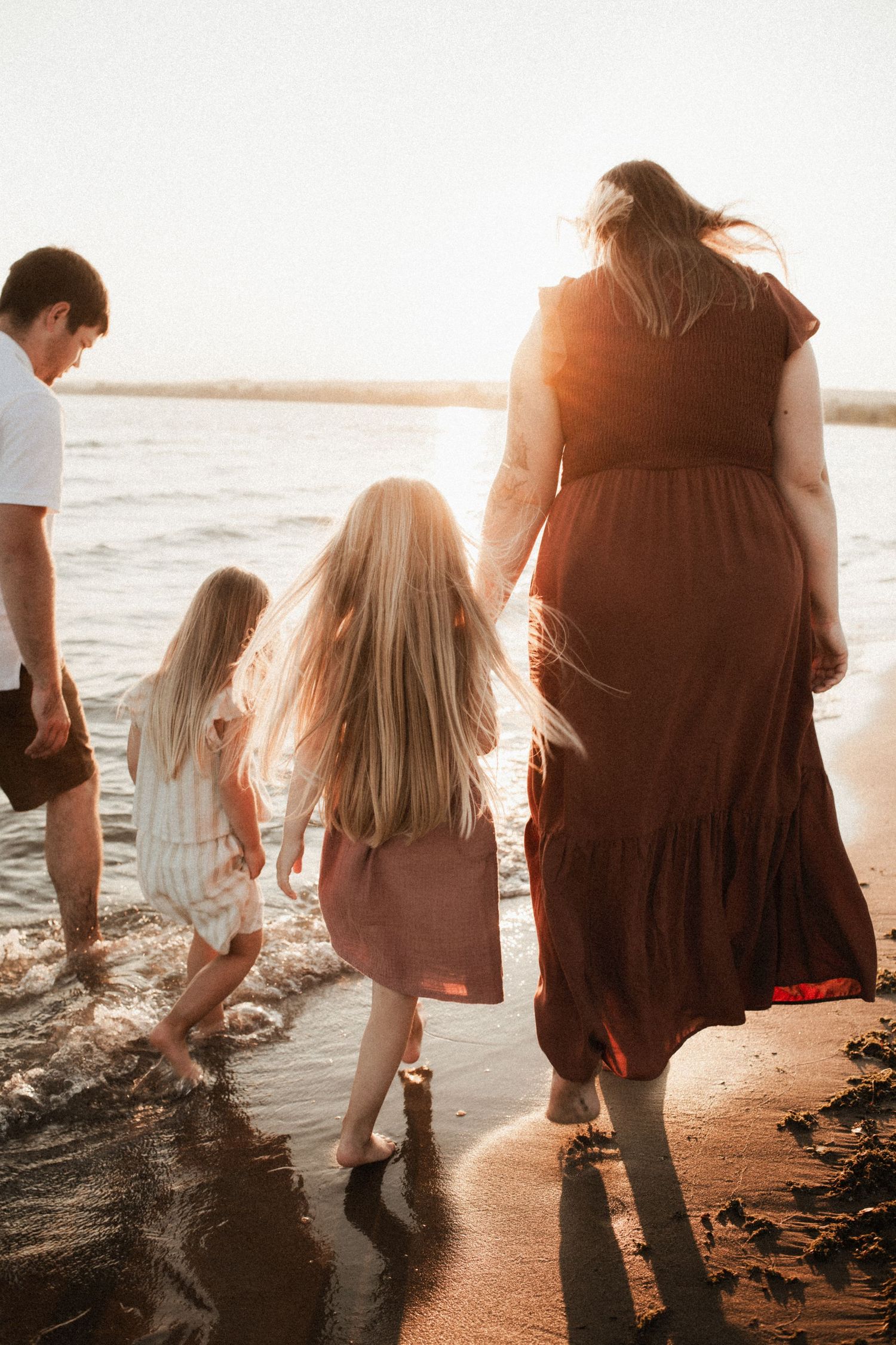 Silhouettes of people walking along a beach shoreline at golden hour.