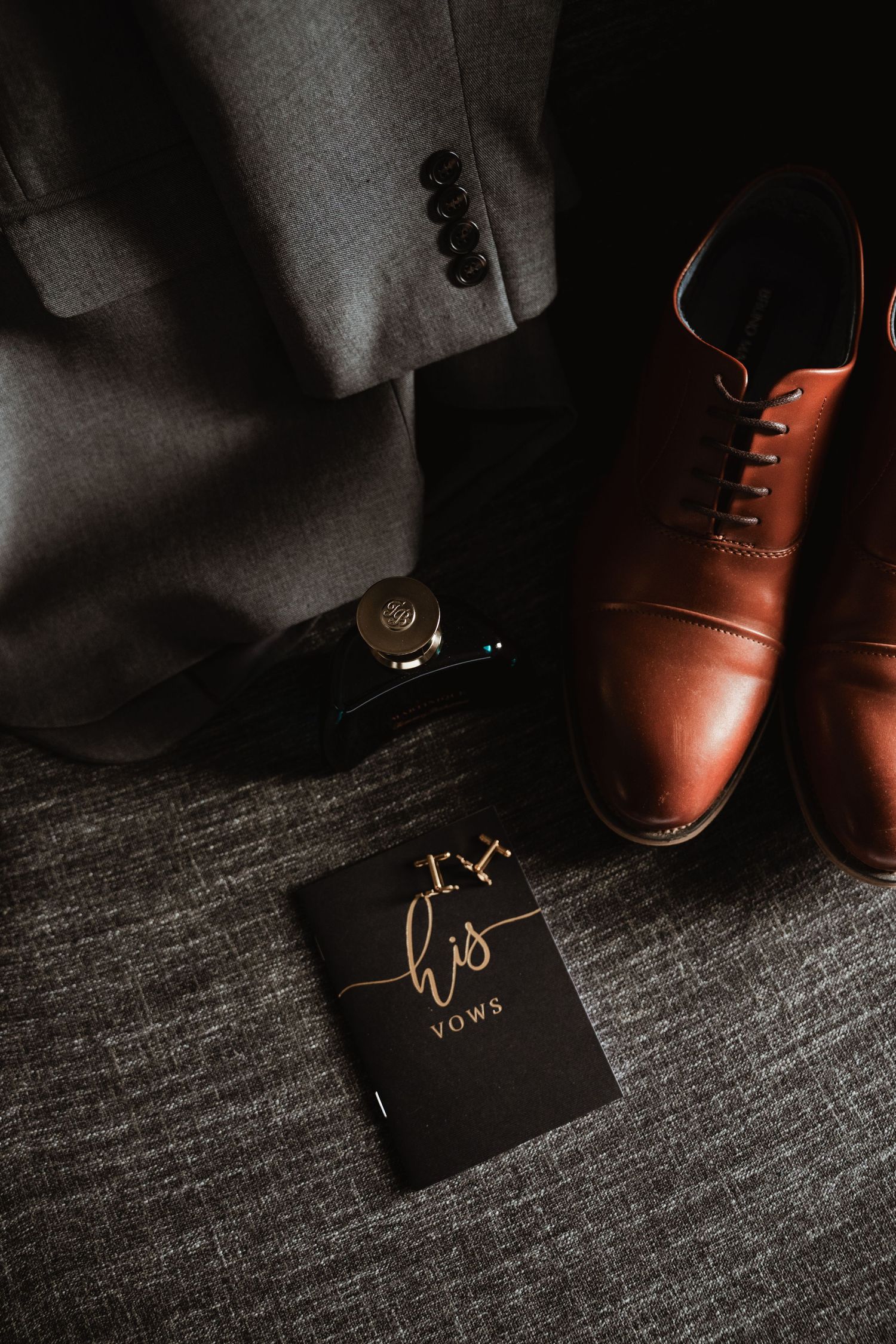 Brown leather dress shoes and vows book arranged on dark textured surface.