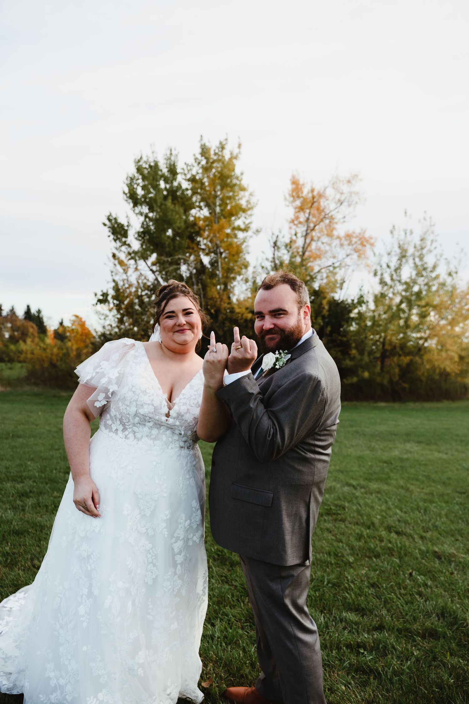 Couple poses playfully for outdoor wedding photos in autumn setting.