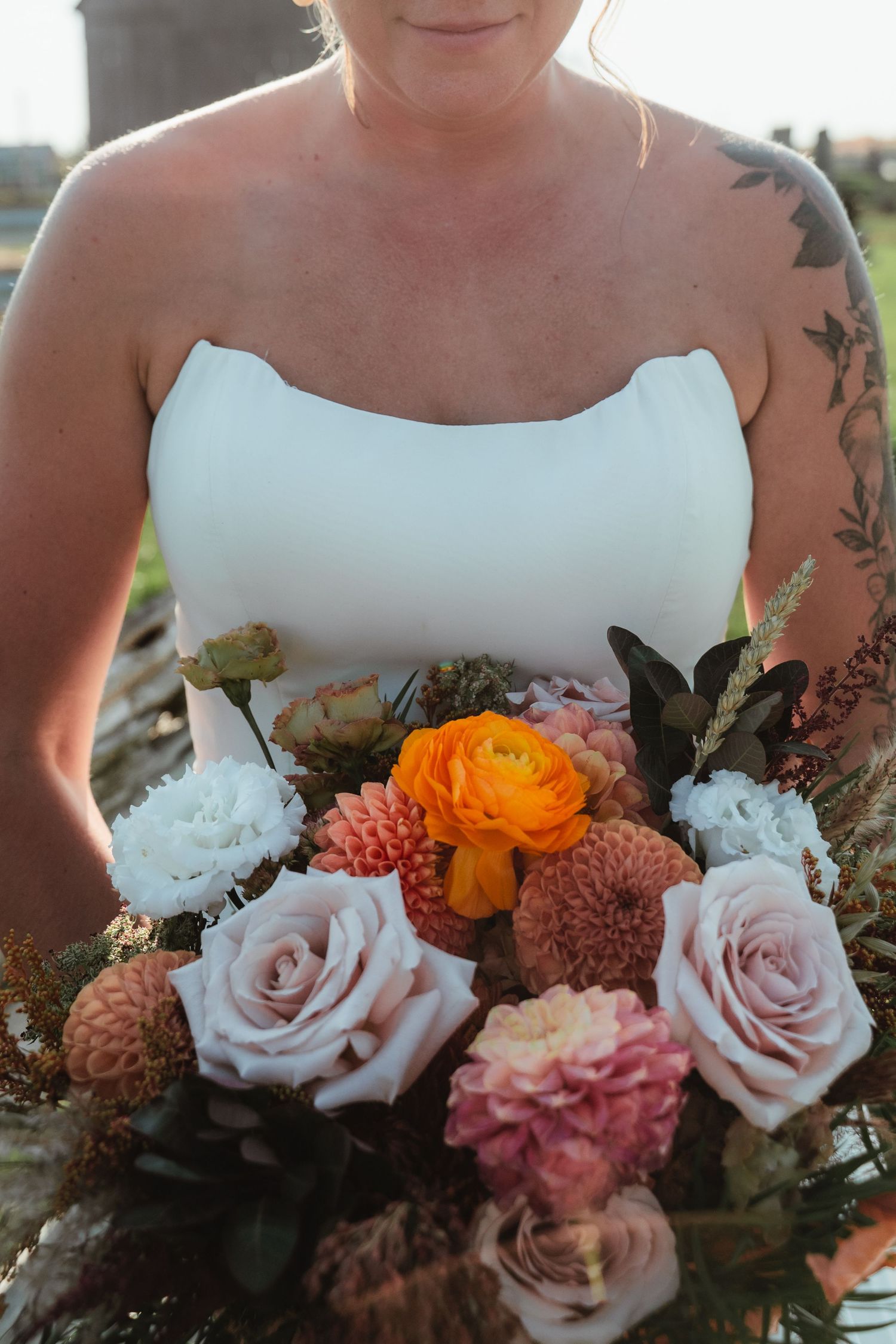 Close-up of bridal bouquet featuring pink roses, orange ranunculus, and mixed flowers.