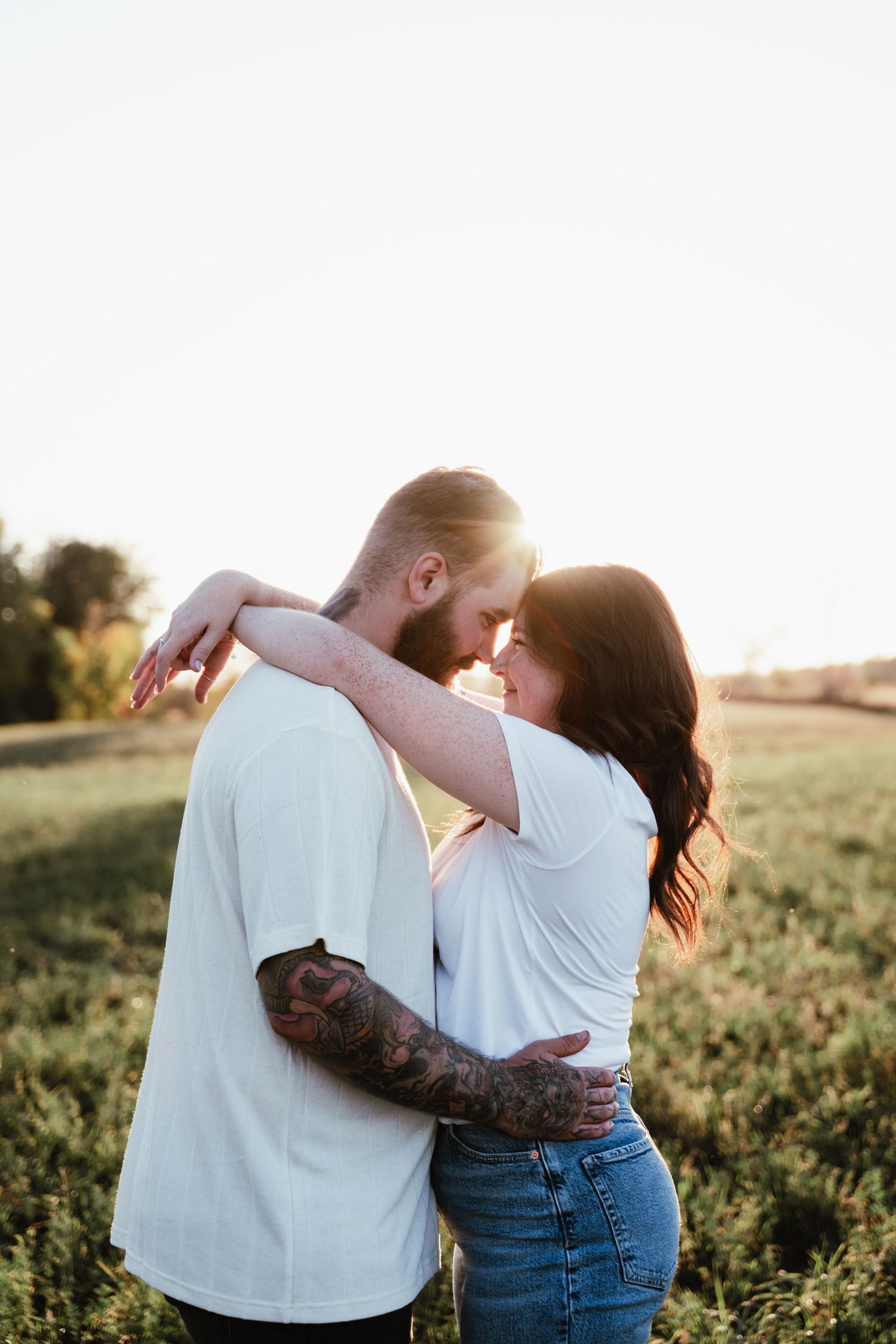 Intimate portrait of couple in white shirts embracing in golden sunlit field.