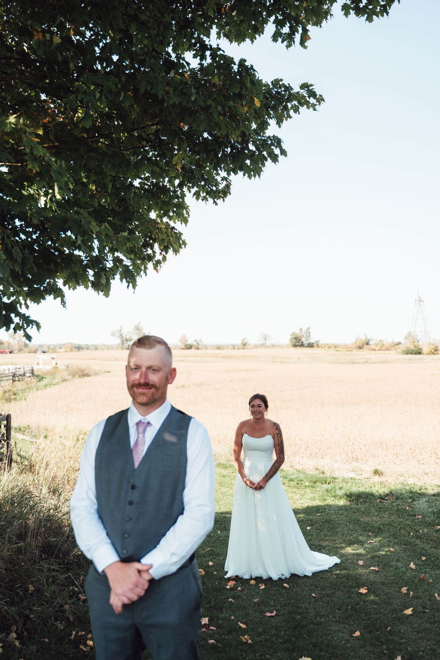 Outdoor wedding first look scene with couple standing apart under tree branches.