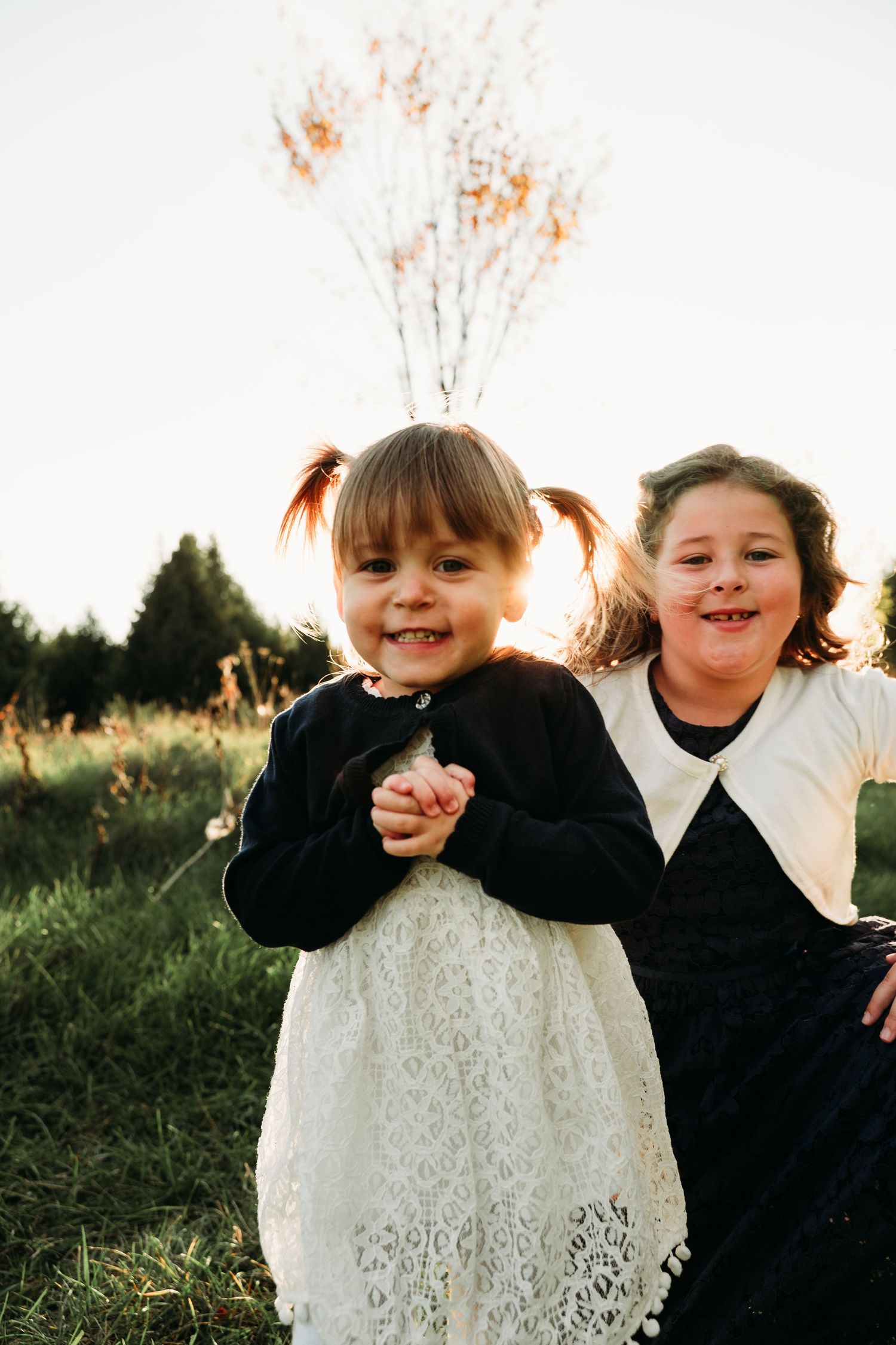 Two children in black and white outfits smile together in golden sunlight.