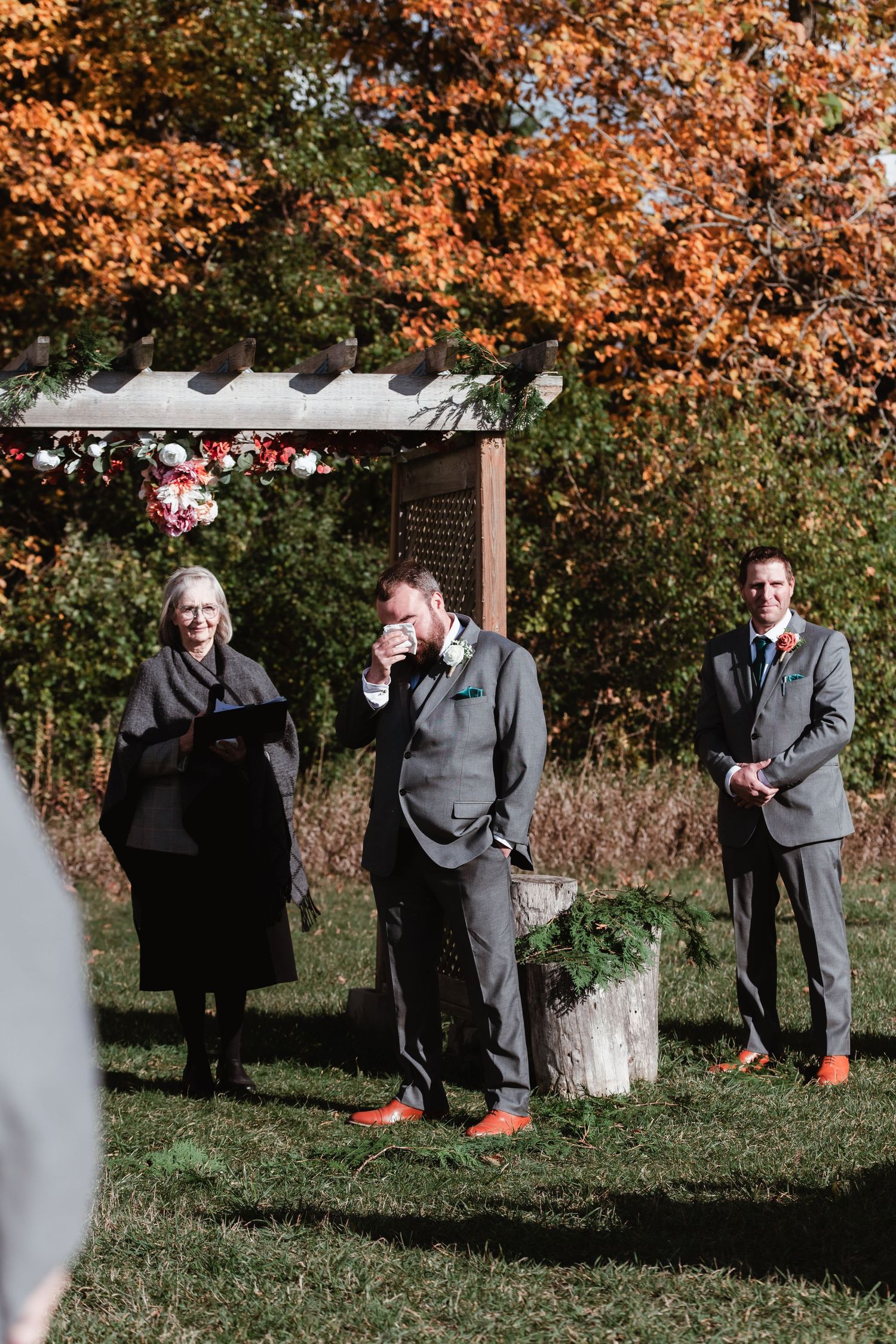 Wedding ceremony setup with autumn foliage and grey-suited attendants.