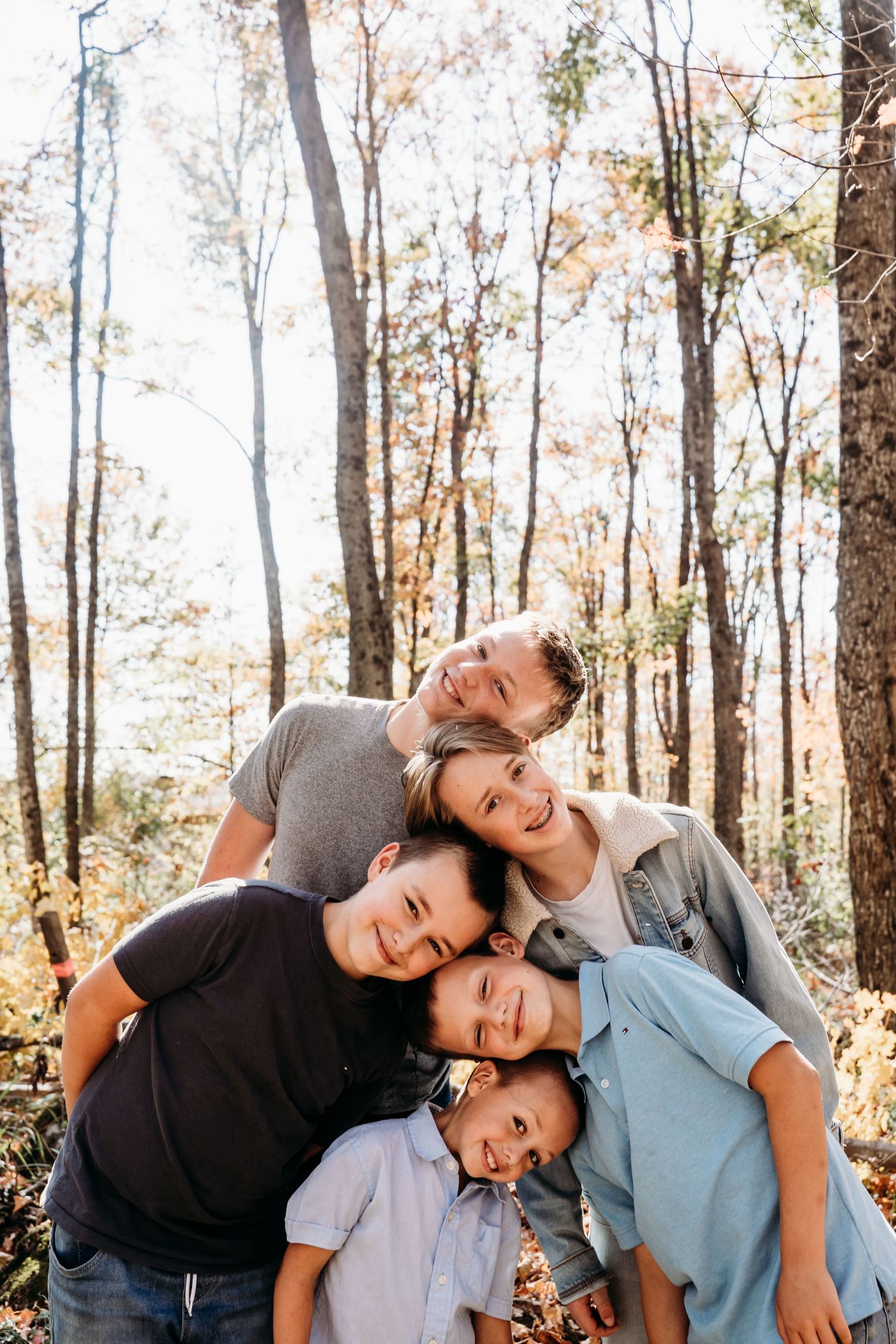 A group poses playfully with stacked heads for a fun family portrait in autumn woods.