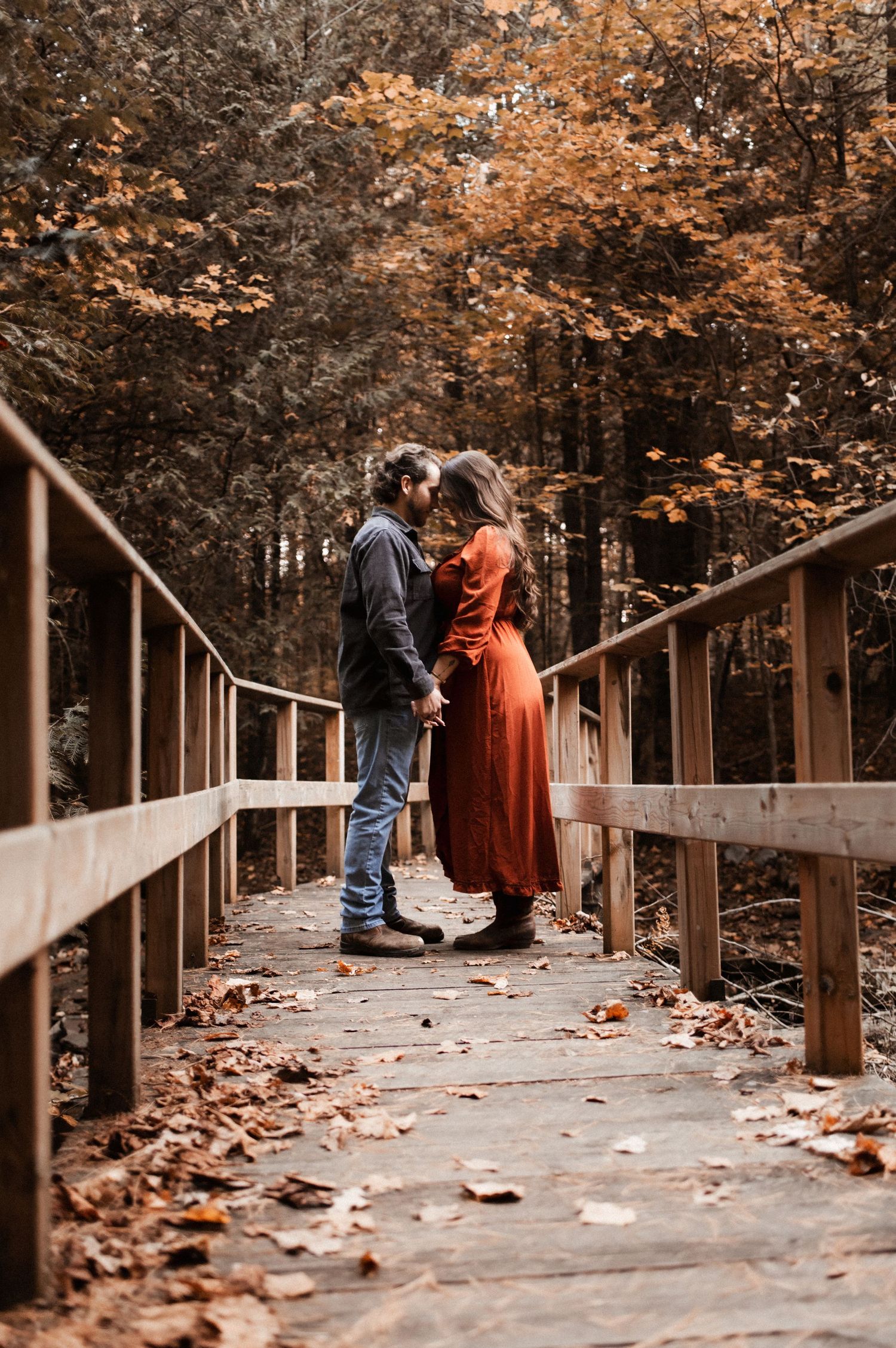 Couple standing on wooden boardwalk surrounded by fall foliage.
