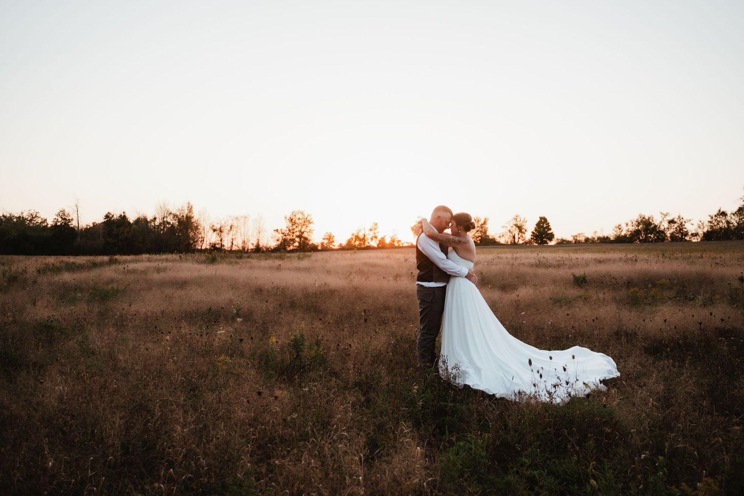 Couple poses dramatically in field during sunset wedding session.