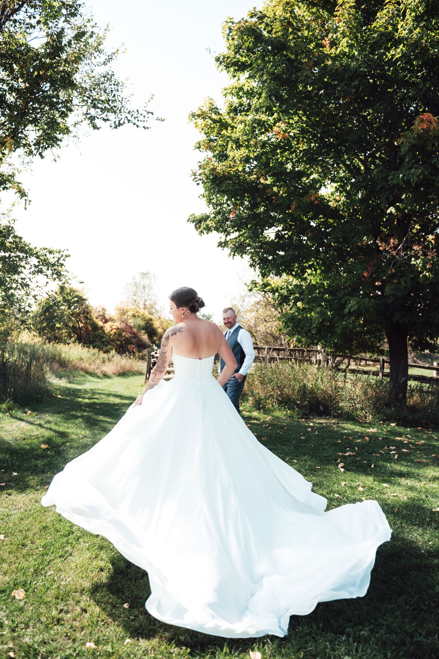 Wedding couple twirling and dancing together under sunlit trees.