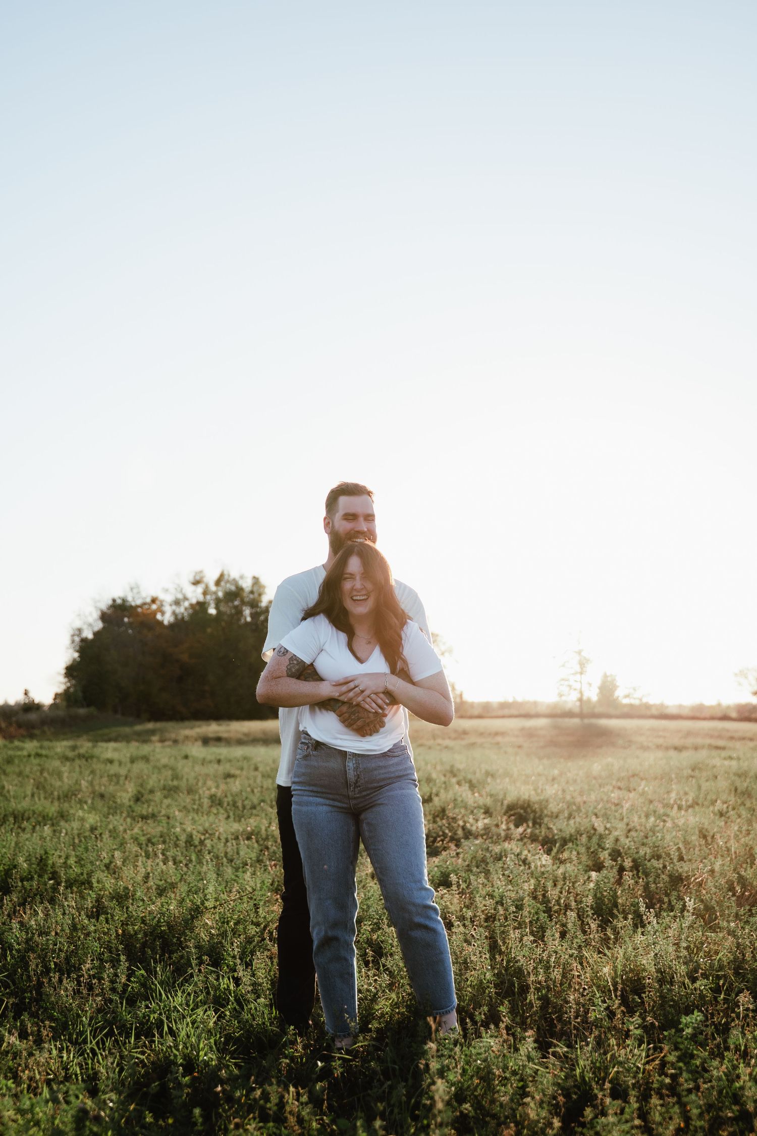 Couple embraces in a sunlit meadow during golden hour, sharing an intimate moment together.