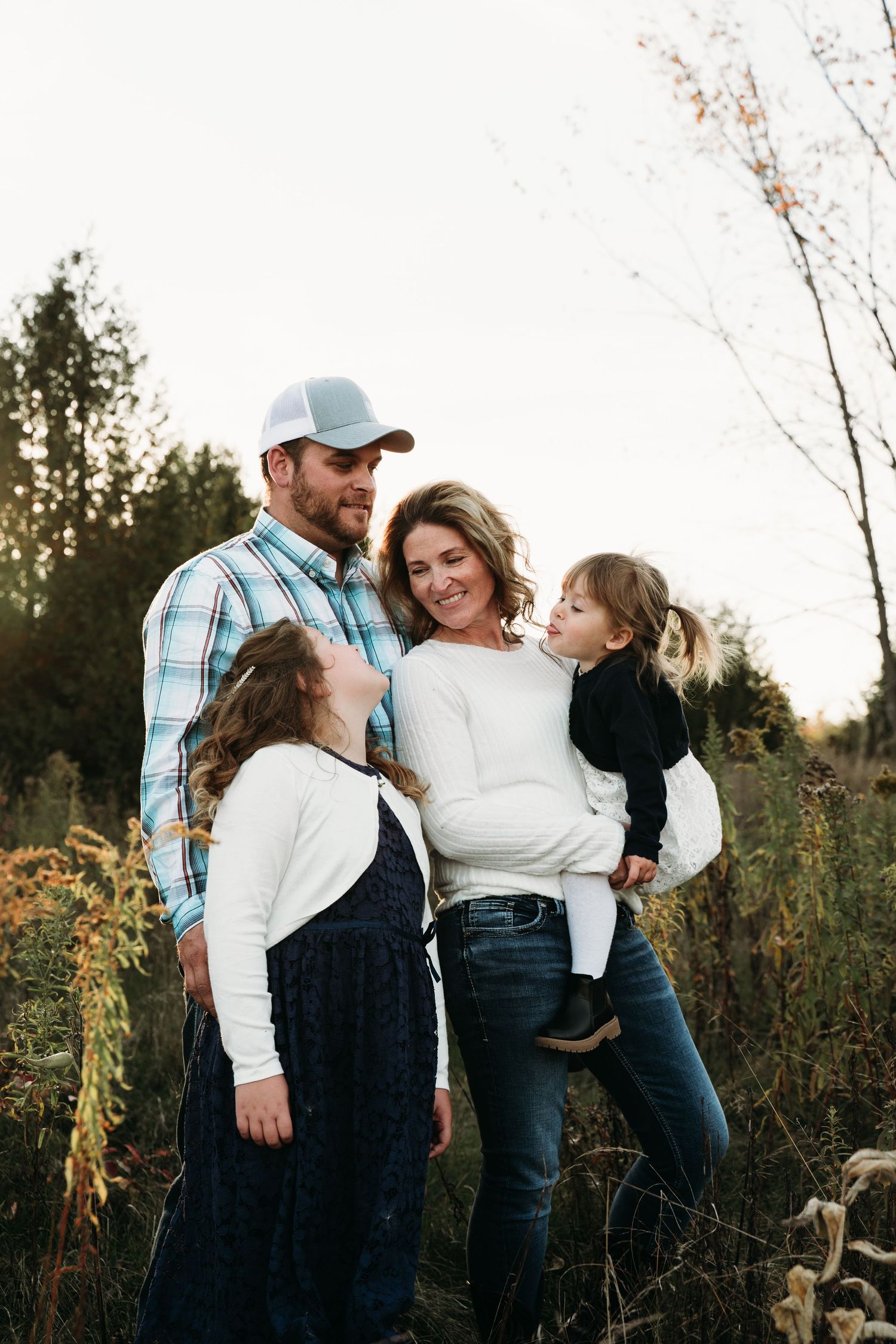 A family of four poses together in a field during golden hour.