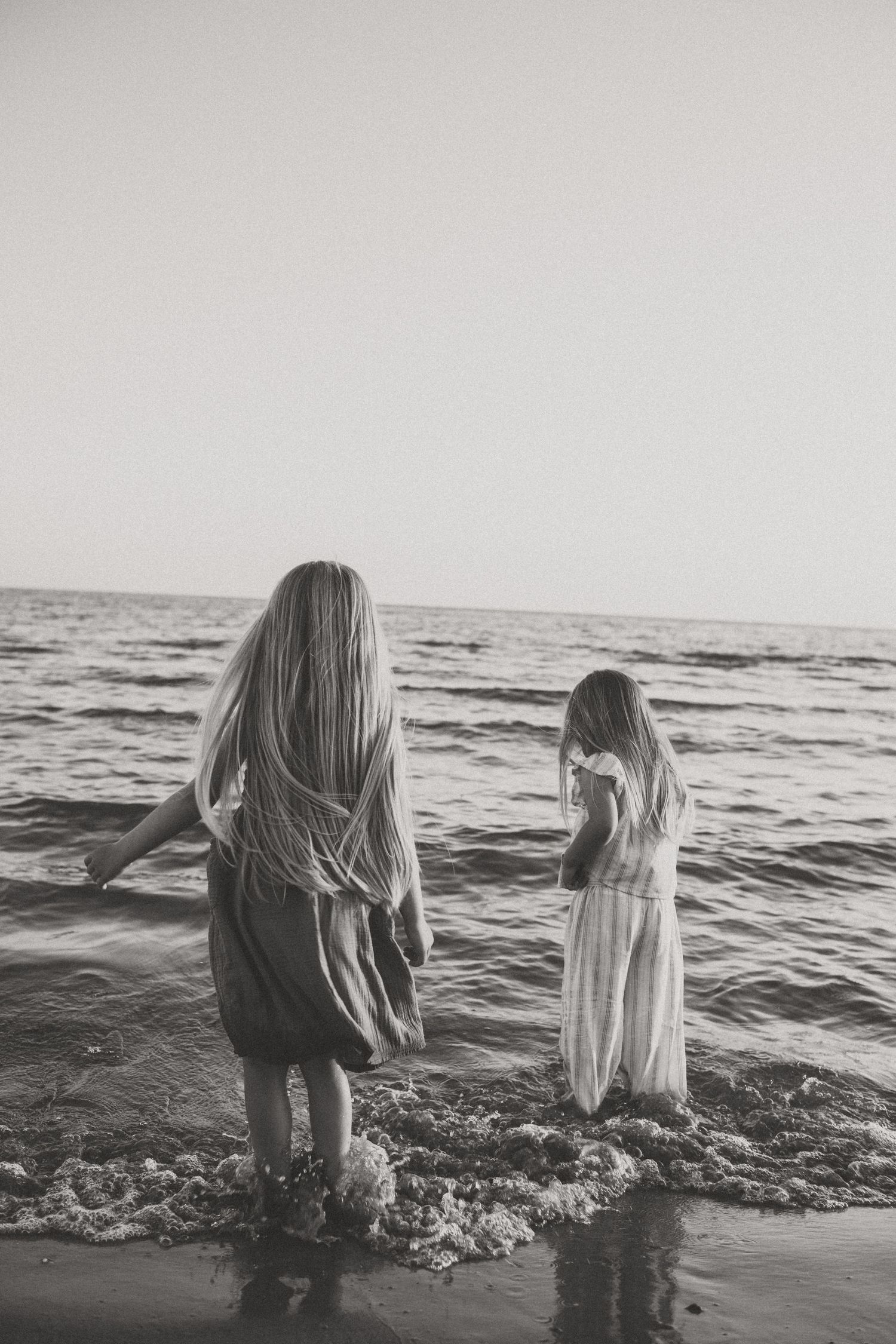Black and white photo of people standing in ocean waves at sunset.