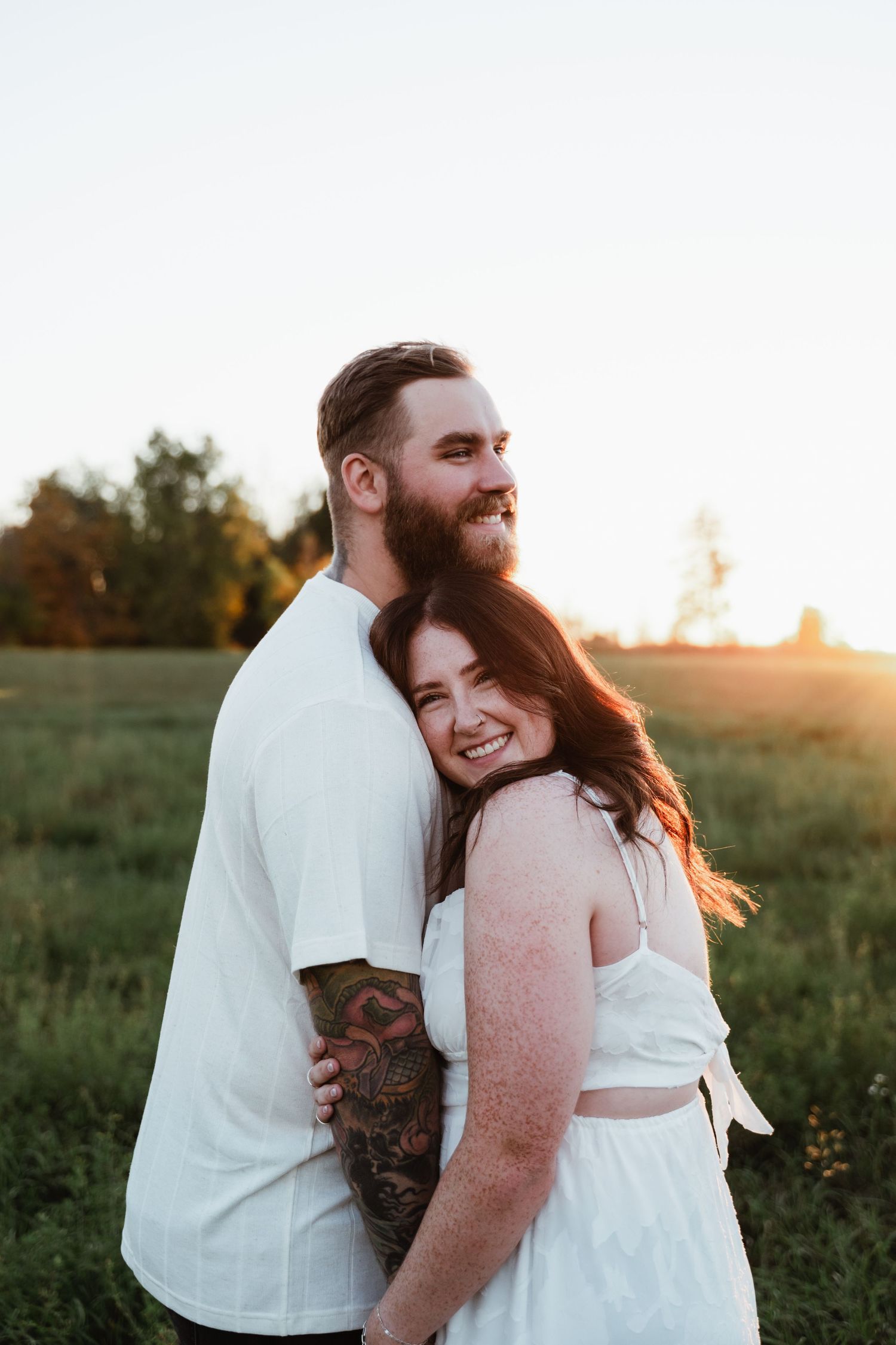 Happy couple in white clothing share warm embrace during sunset photoshoot.