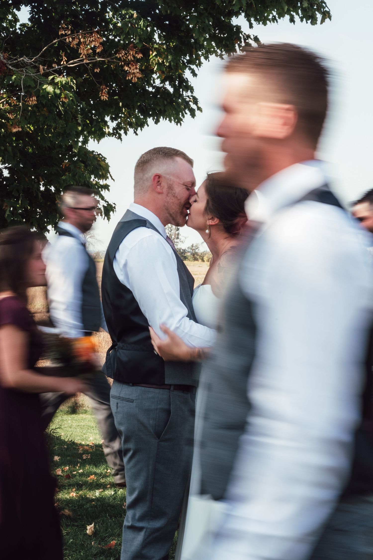 A motion-blurred wedding celebration photo with guests moving through an outdoor garden setting.