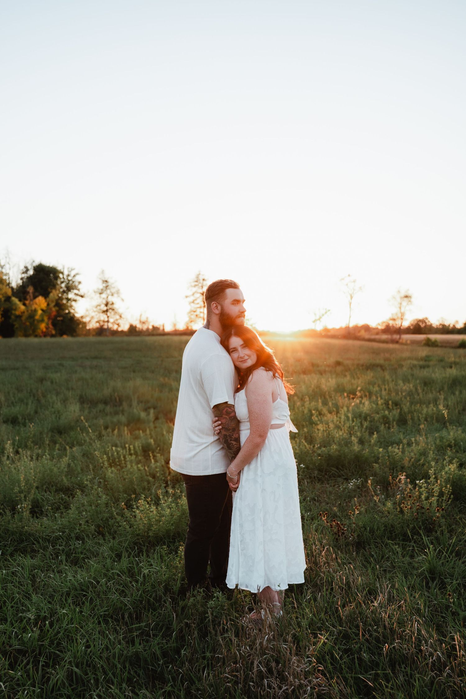 Romantic sunset portrait of couple standing together in white outfits against golden light.