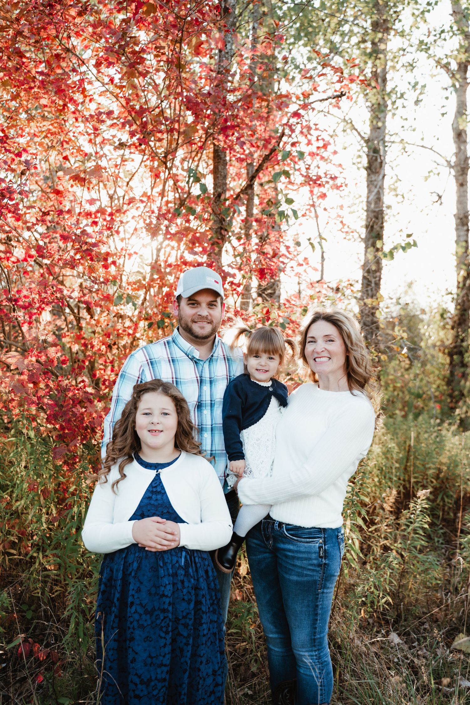 Family group portrait against vibrant red autumn foliage.