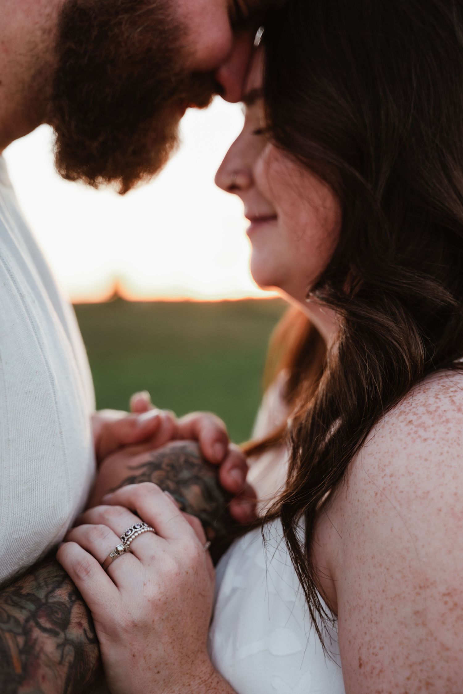 Close-up of couple's intimate moment showing engagement ring during sunset photoshoot.