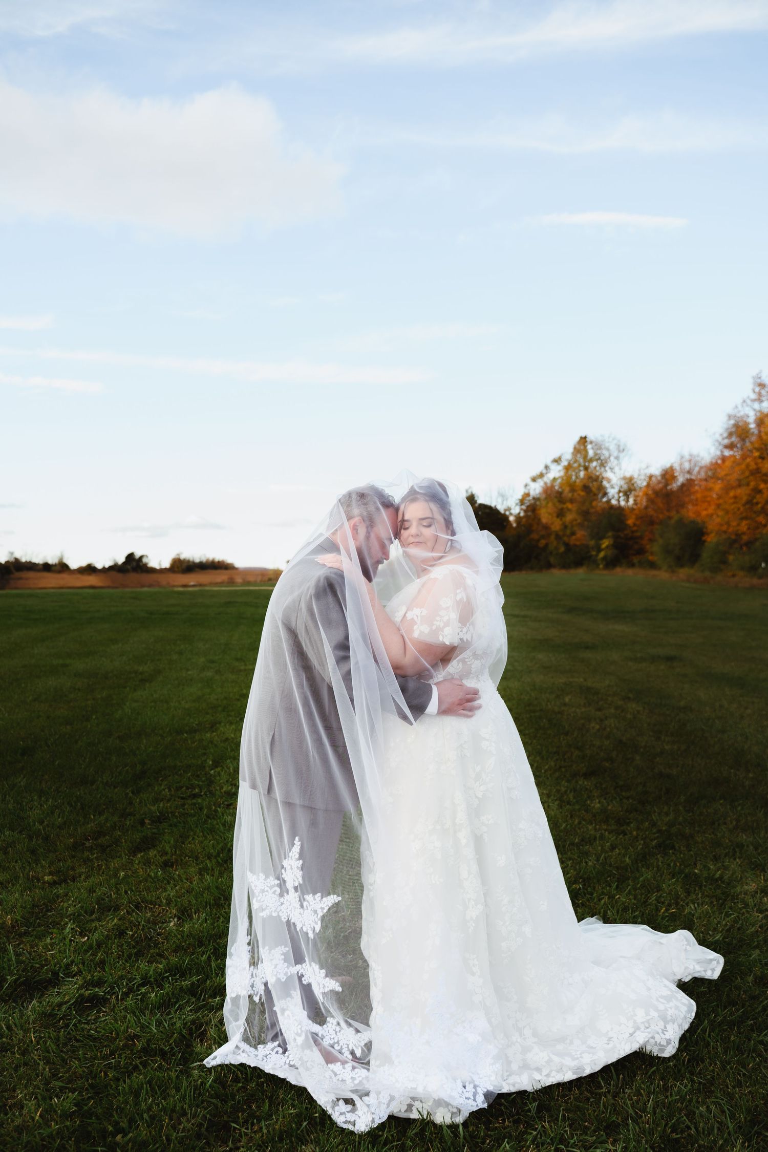 Couple shares intimate moment under flowing veil in autumn field.