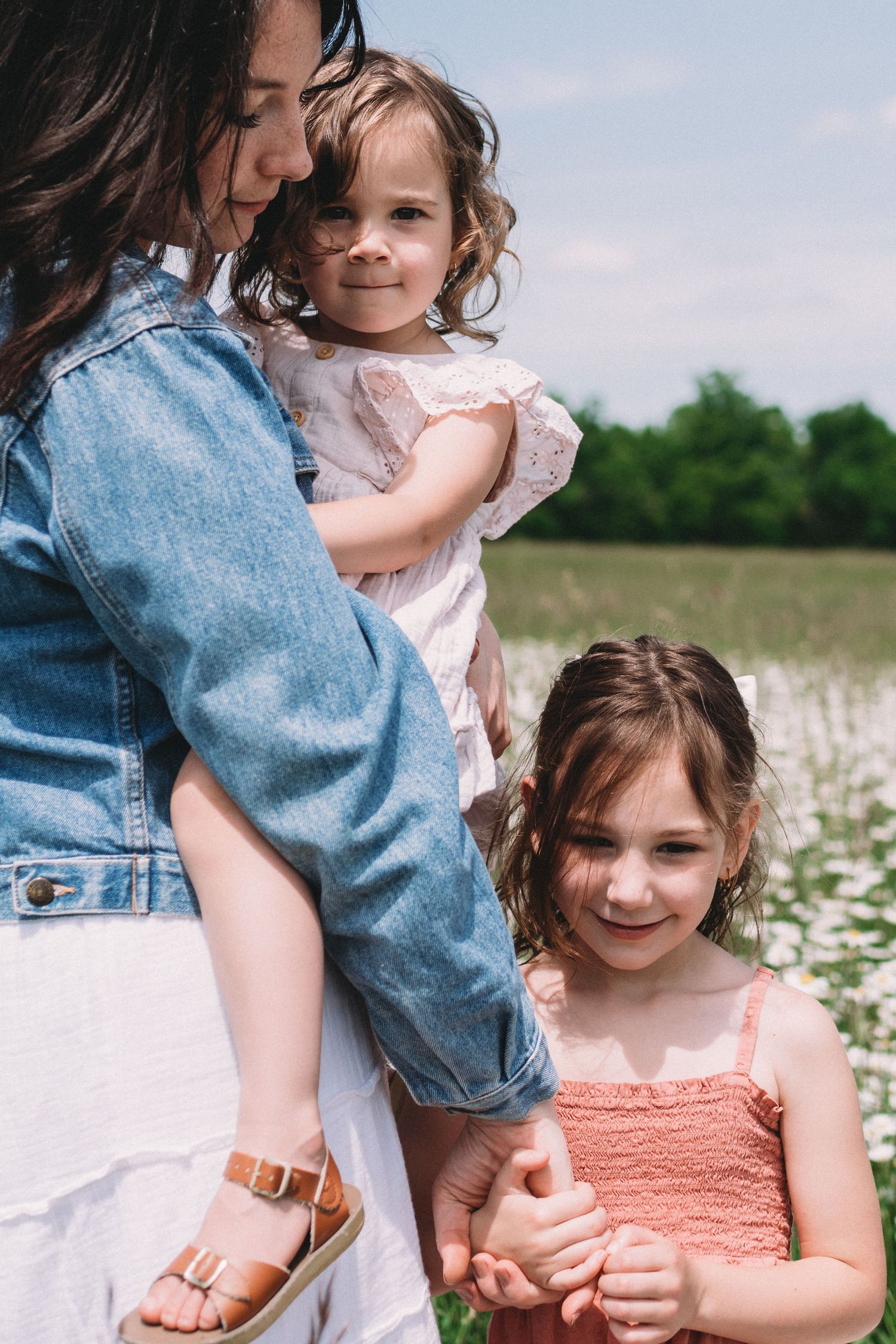 A tender moment captured in a field with denim and floral dresses on a sunny day.