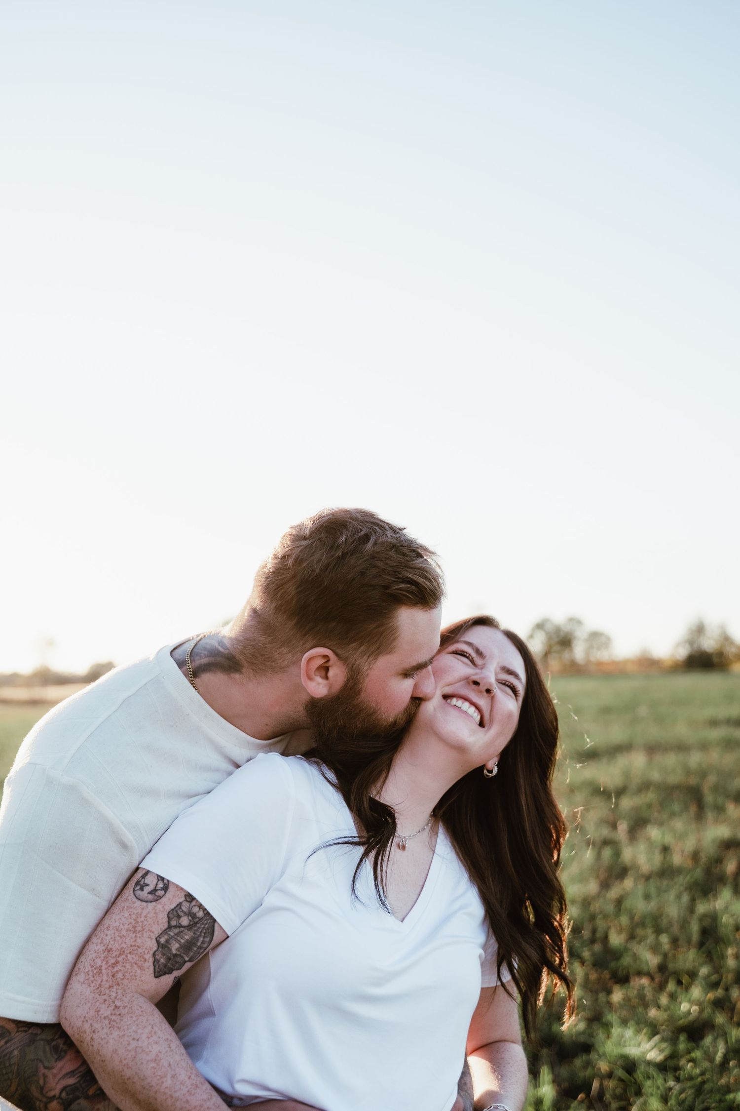 Couple laughing and embracing in a field at sunset with joyful expressions.