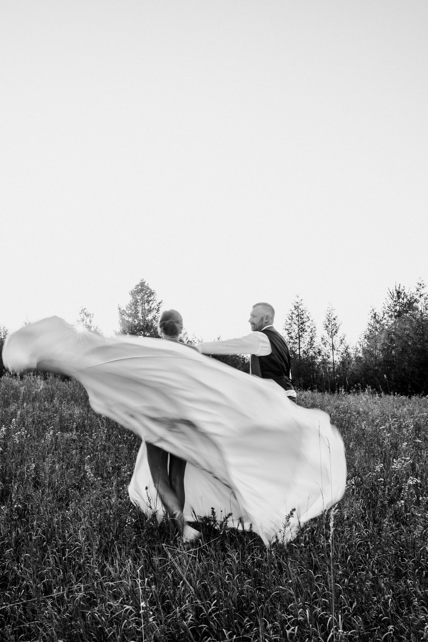 A dramatic black and white wedding photo with flowing dress in a meadow.