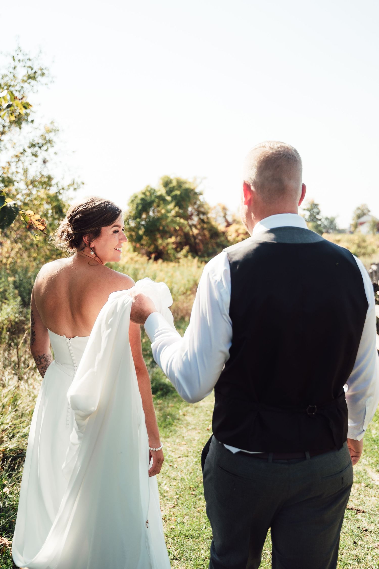 A bride in a flowing white dress and groom in a vest share an intimate moment outdoors on their wedding day.