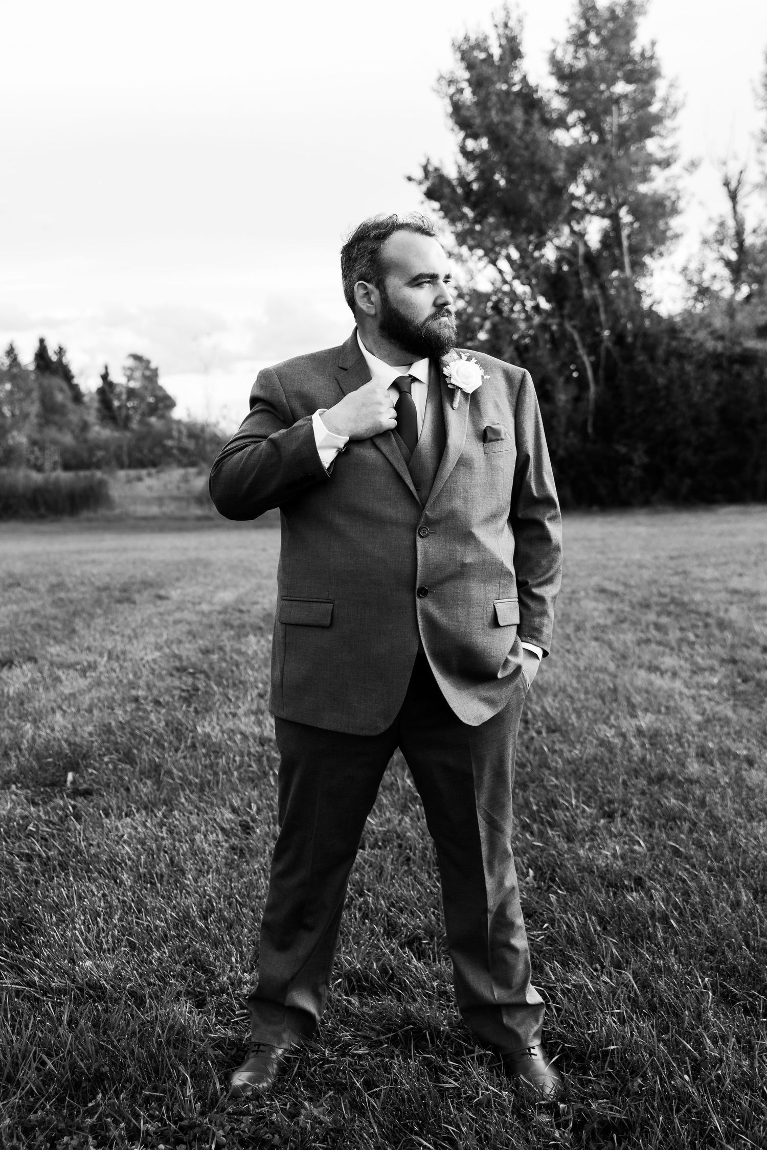 Black and white photo of groomsmen posing casually in a grassy field.