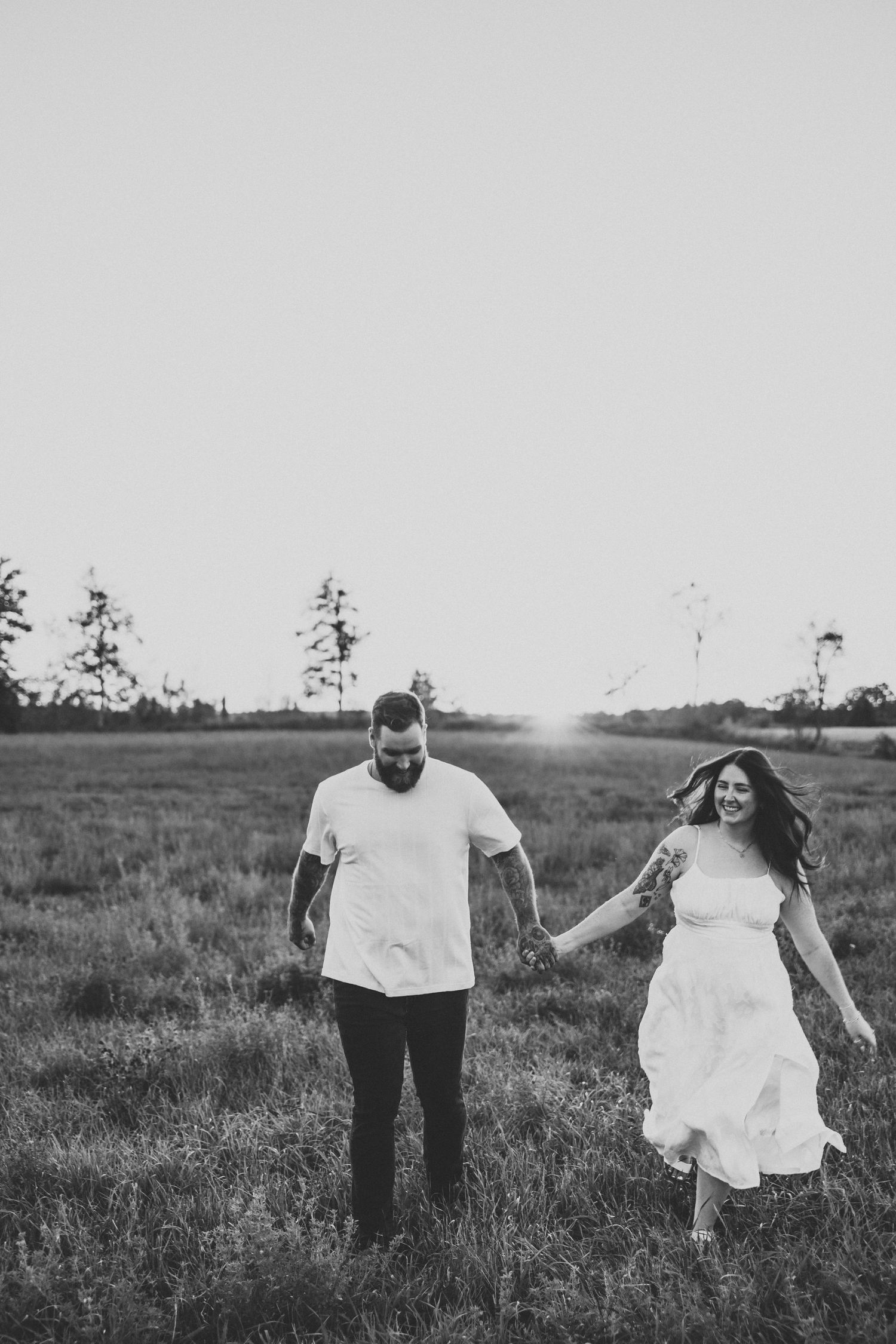 Couple in white clothing walking hand in hand through meadow at sunset.