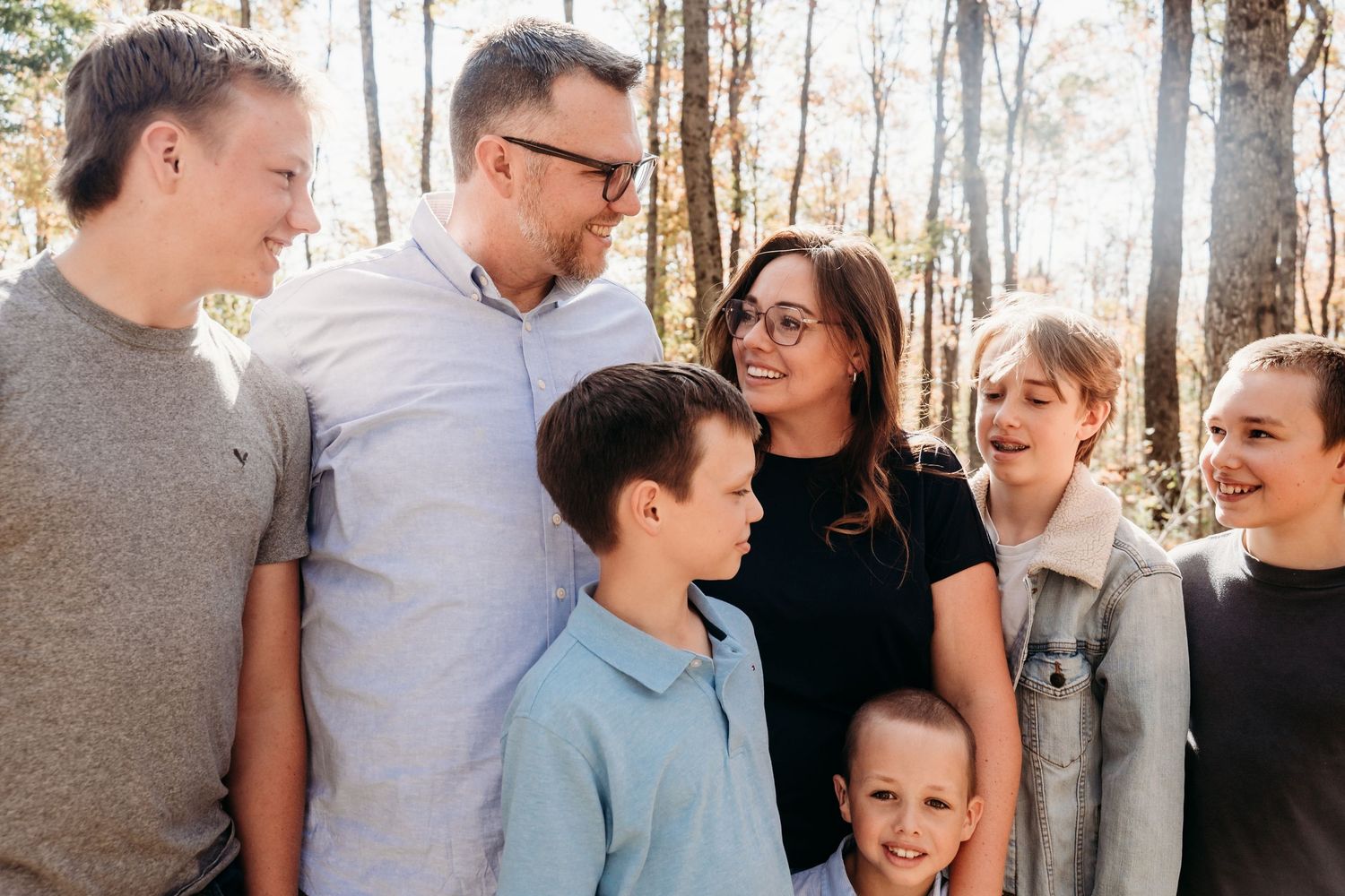 A group poses together for a casual outdoor family portrait in a wooded setting.