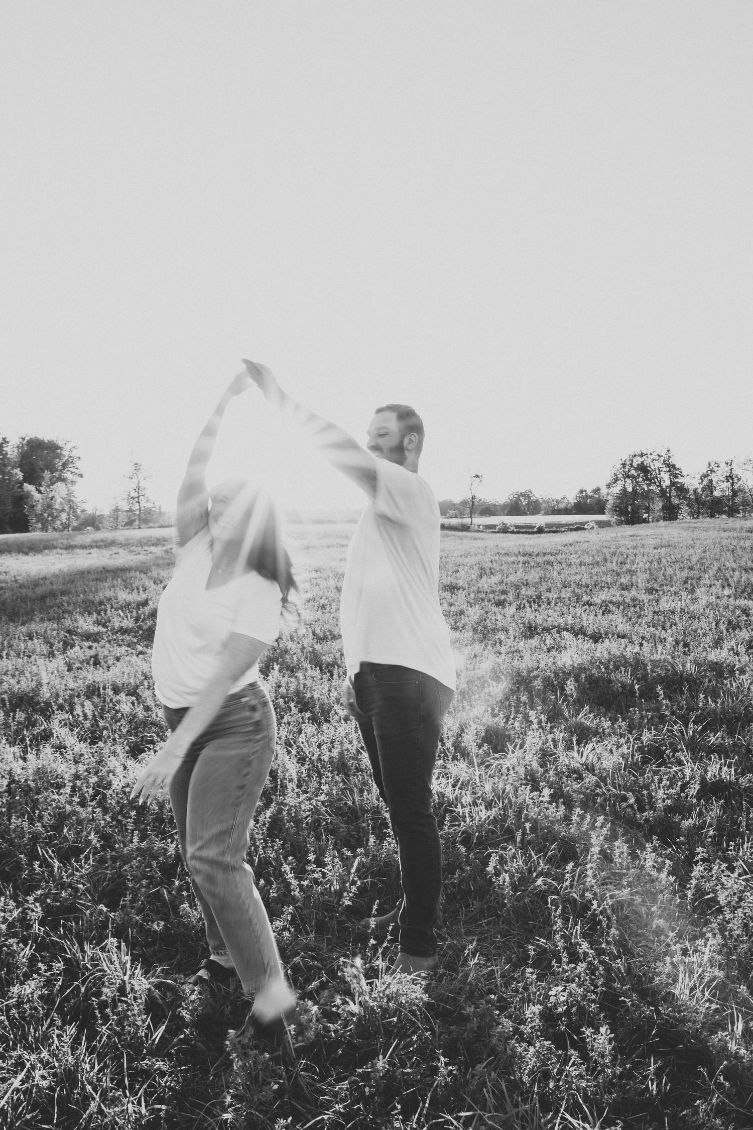 Black and white photo of couple dancing and spinning in a sunny meadow.
