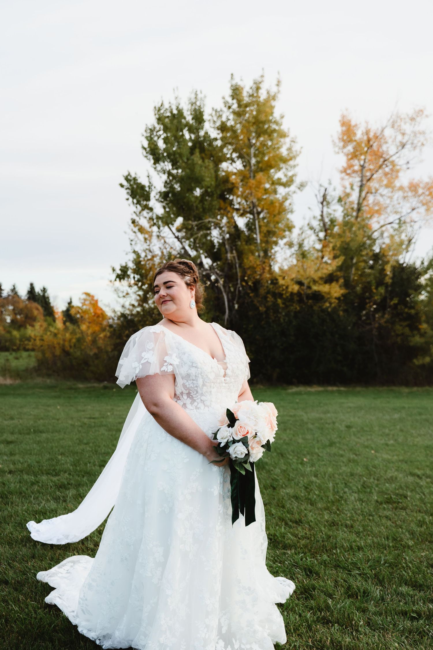 Bride in lace wedding dress poses gracefully in outdoor autumn setting.